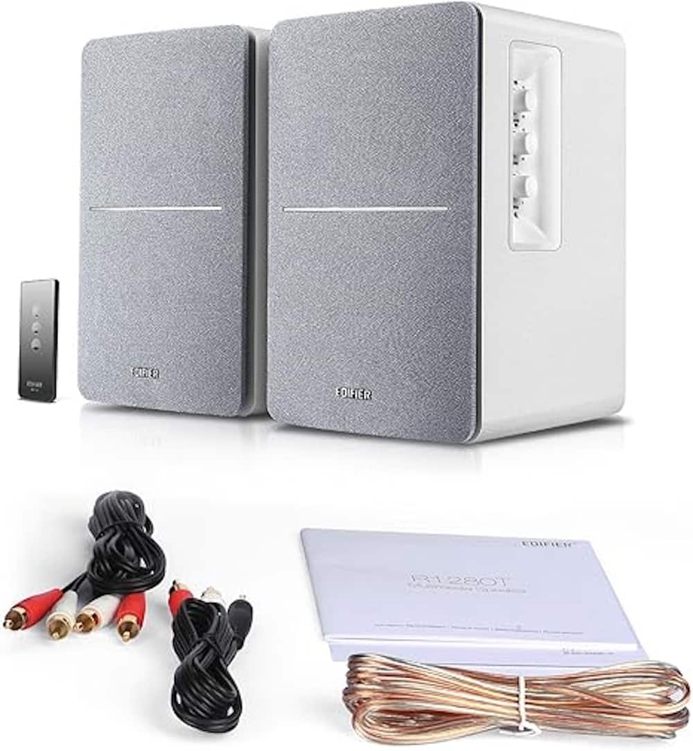 The image features a pair of Edifier speakers, which are white and gray in color. They are accompanied by a remote control and a set of cords. The speakers are placed next to each other, and there is also a manual and a warranty card included in the package. The overall setup suggests that the speakers are ready to be set up and used.