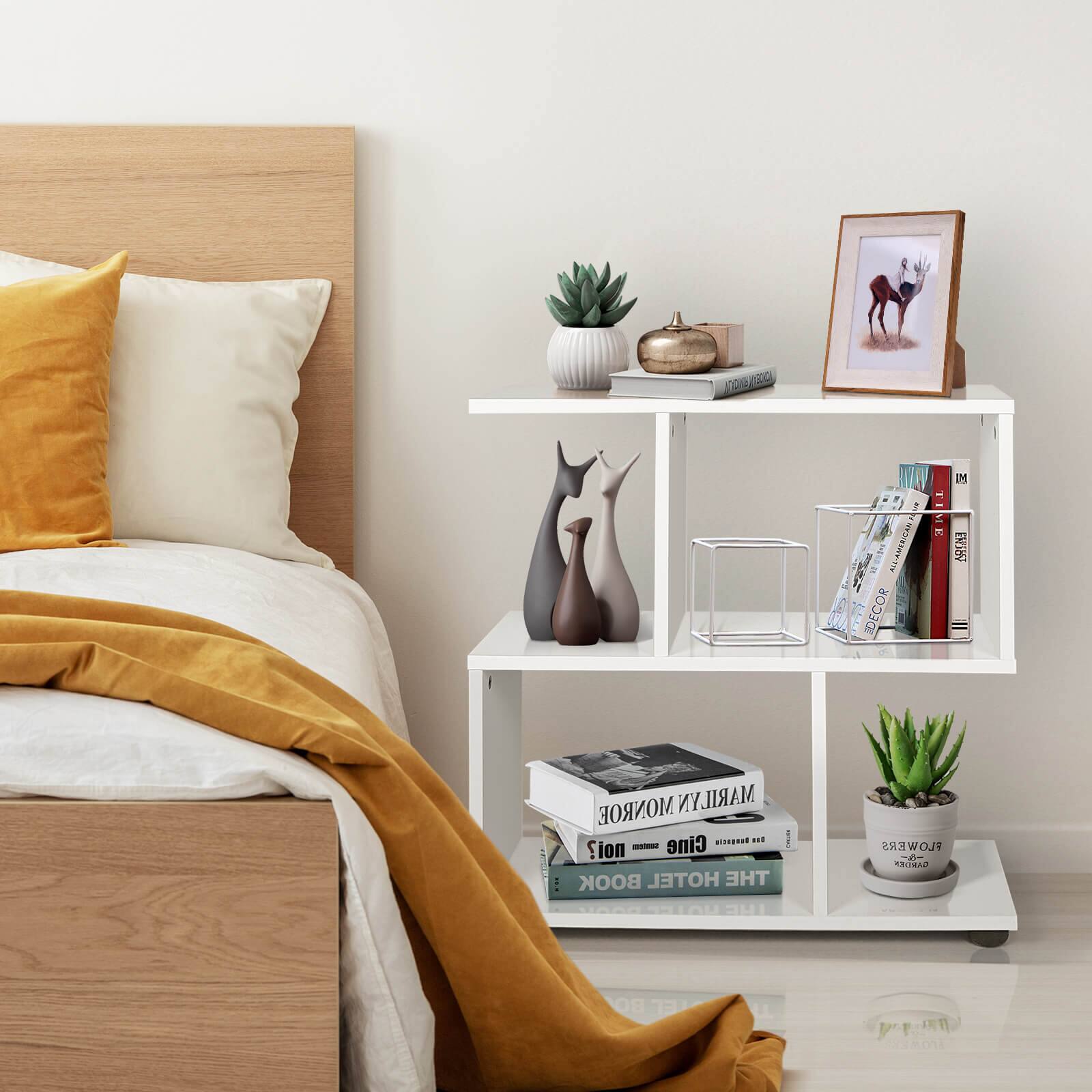The image features a bed with a yellow blanket and a white pillow. Next to the bed, there is a white shelf with various items on it, including a vase, a picture, a book, and a potted plant. The shelf also has a small statue of a cat on it. The scene creates a cozy and inviting atmosphere in the bedroom.