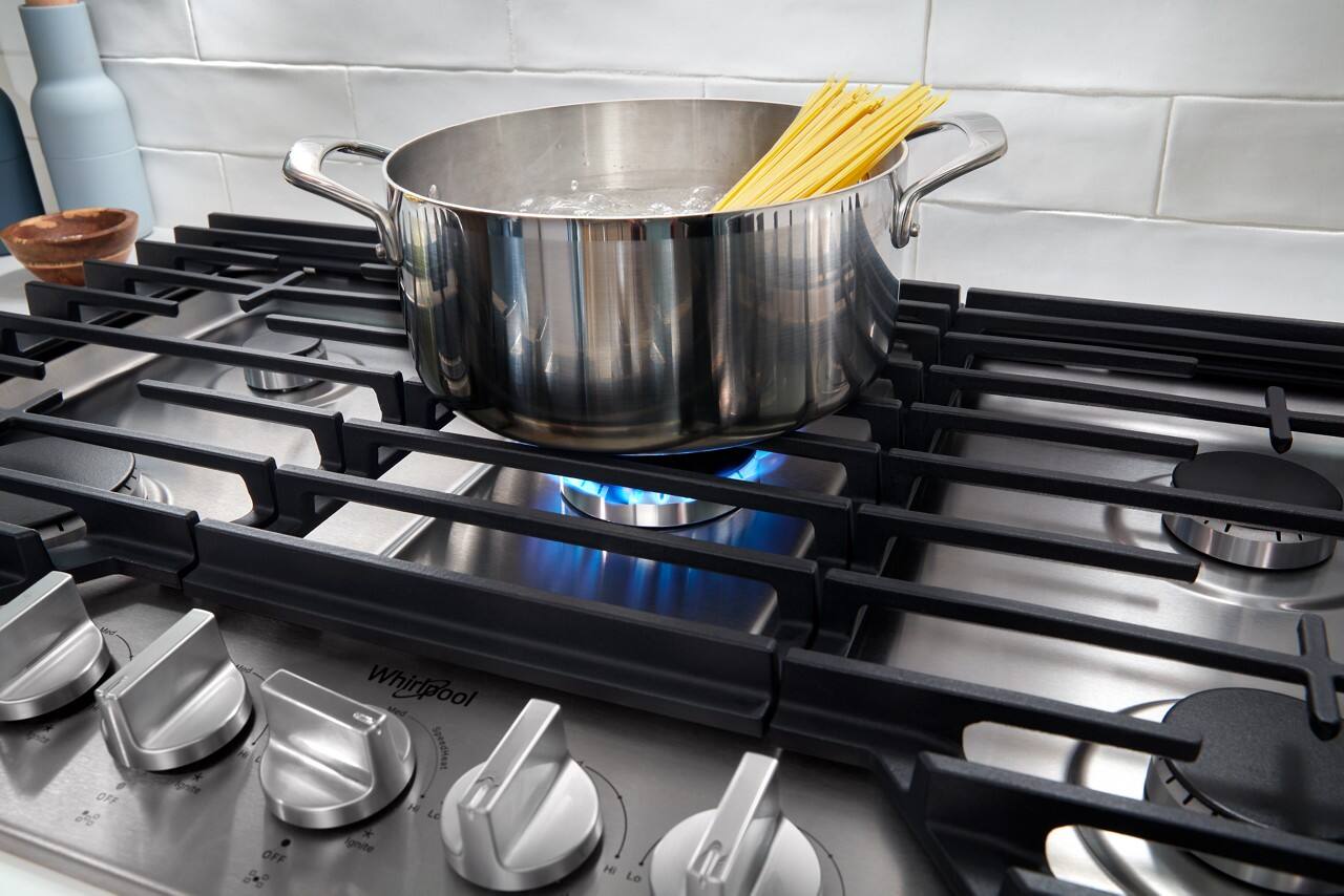 The image shows a pot of water on a stove, with a spoon in it. The stove has a black knob, and the pot is placed on the burner. The stove is turned on, and the pot is filled with water. The spoon is likely being used to stir or cook the contents of the pot.