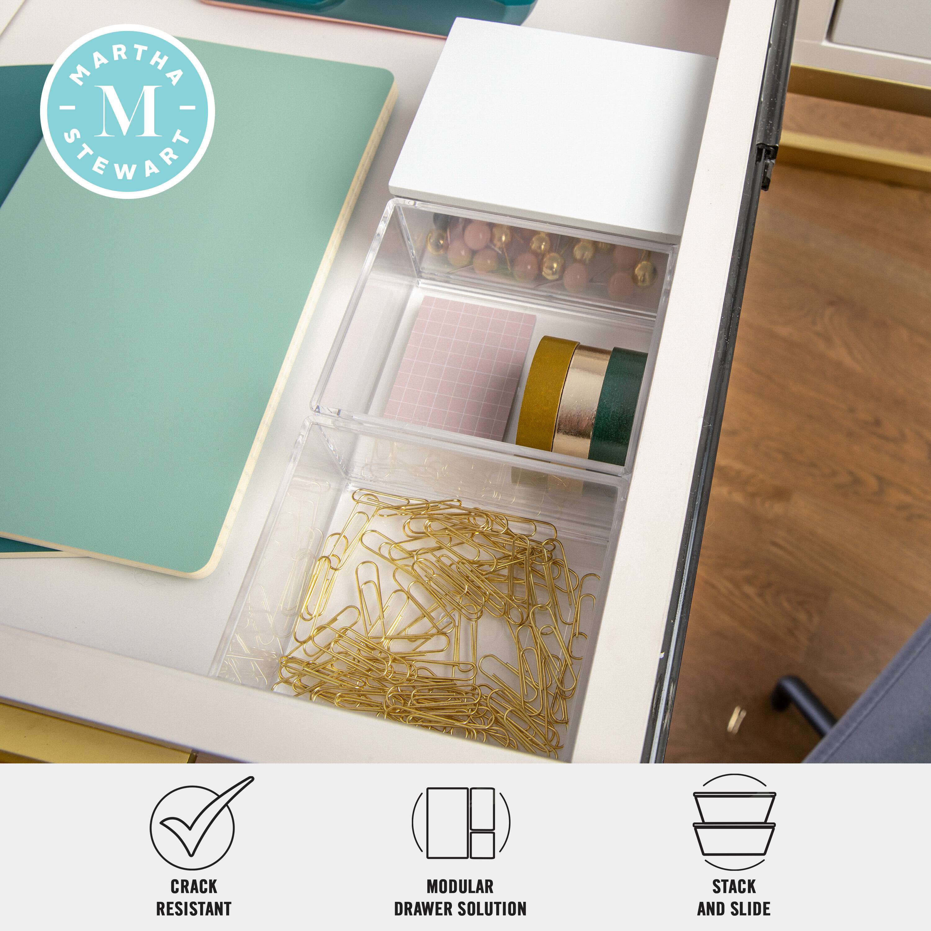 The image features a desk with a drawer open, revealing a variety of items such as pins, scissors, and paper clips. The drawer is part of a Martha Stewart modular drawer solution, which is designed to provide a practical and organized storage solution for office supplies. The drawer is also advertised as being crack resistant, ensuring that the items stored within remain secure and undamaged.