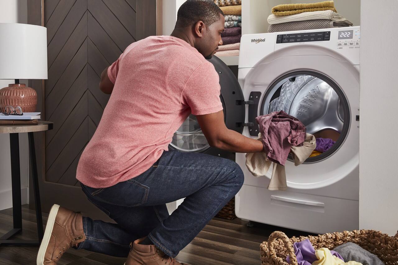 The man is kneeling down in front of a Whirlpool washing machine.