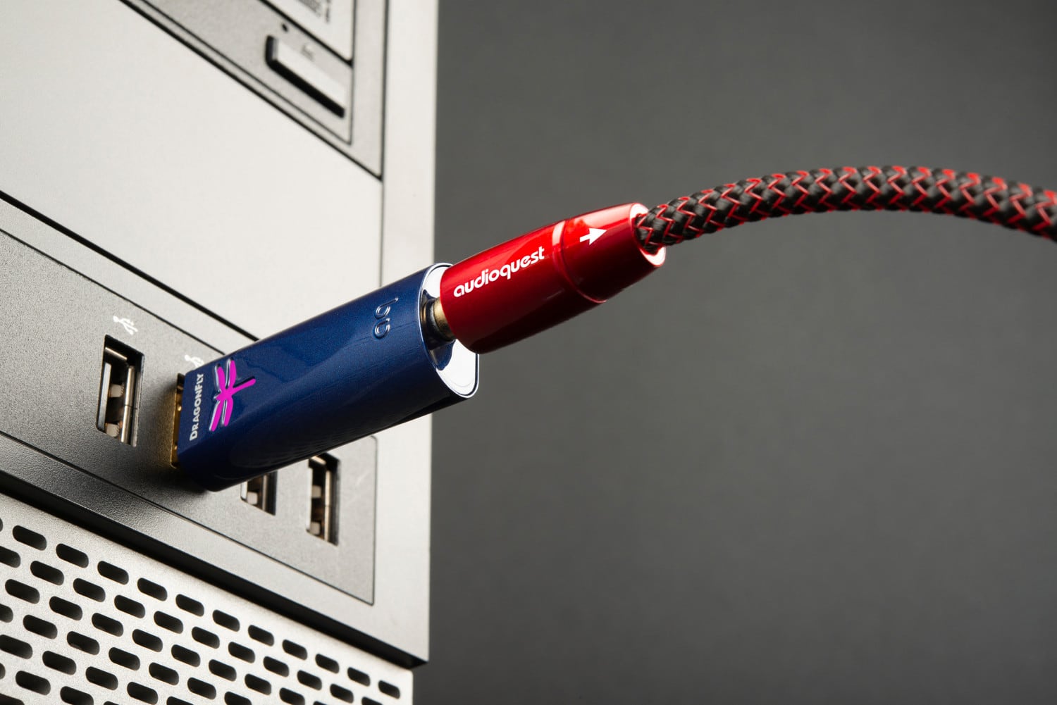 The text on the image reads "DR DRAGONFLY * bo audioquest." This is likely a product name or brand name for an audio device, such as a sound card or headphones. The red and black cords are connected to the device, which is plugged into a computer.