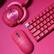 The image shows a pink keyboard and mouse on a pink background. The keyboard has a pink and red color scheme, and the mouse is also pink. The keyboard is placed next to the mouse, and both are sitting on a pink surface.