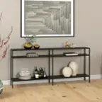 The image features a shelf with various items on it. There are multiple bottles, a vase, and a bowl placed on the shelf. Additionally, there is a picture hanging on the wall above the shelf. The shelf is situated on a wooden floor, and a potted plant can be seen nearby.