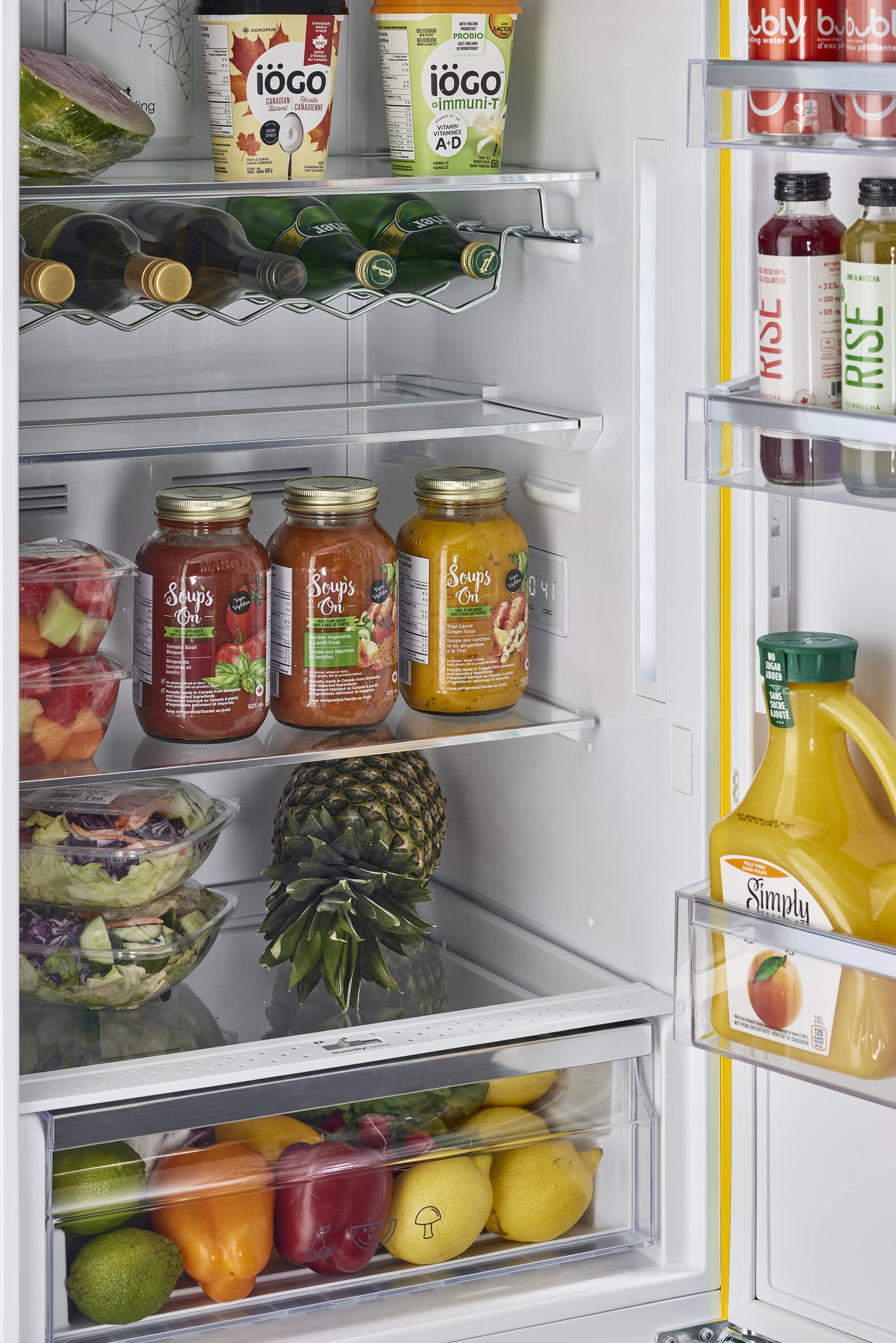 The refrigerator is stocked with a variety of food items, including fruits, vegetables, and drinks. There are several bottles of juice, such as orange juice, and a bottle of milk. The refrigerator also contains a bowl of fruit, which includes apples and oranges. Additionally, there are multiple bottles of water and other beverages. The refrigerator is well-organized, with the food items placed in their respective compartments, making it easy to find and access the desired items.