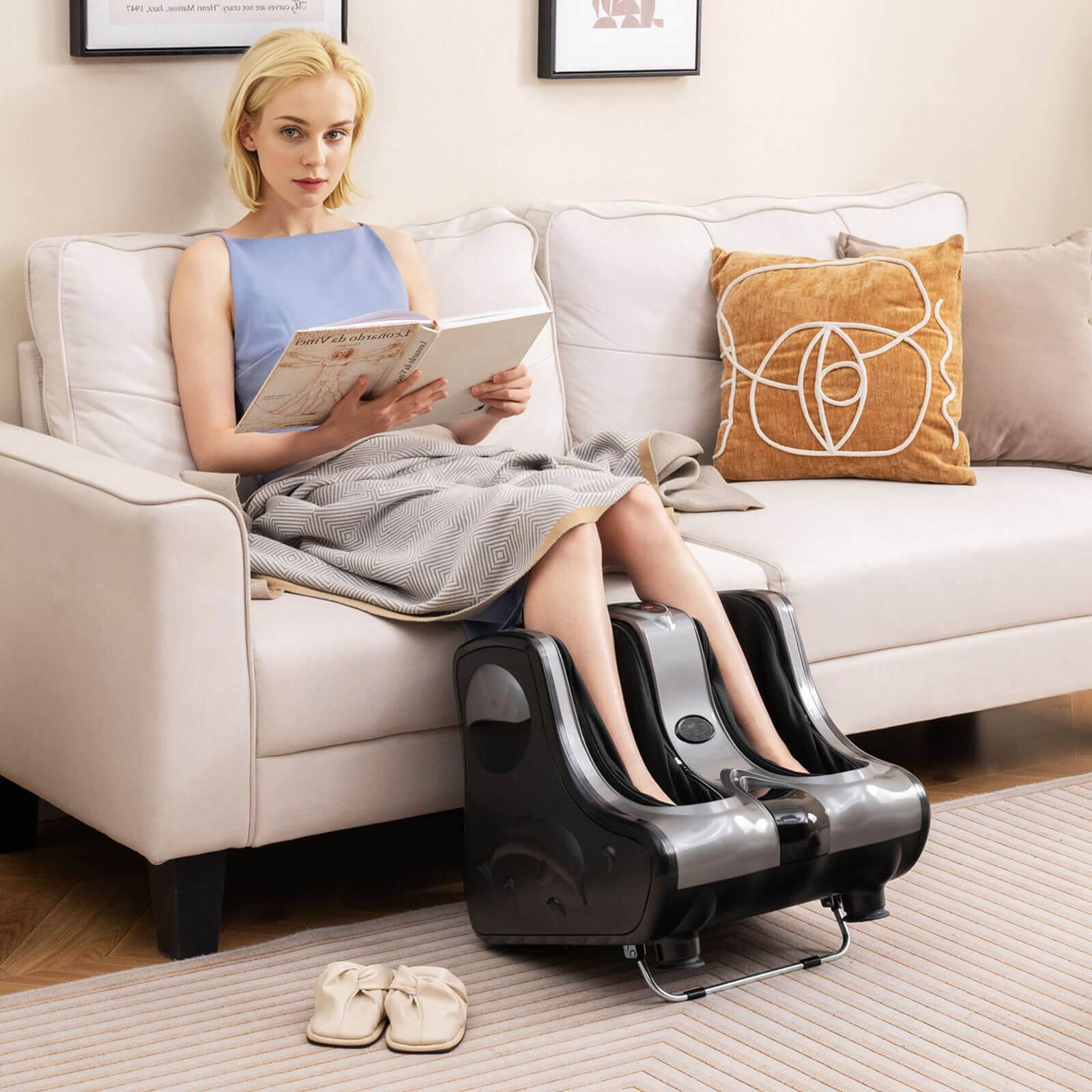 The image shows a woman sitting on a couch, wearing a pair of black boots and reading a book. She is also wearing a pair of black boots that are attached to a machine. The couch is white, and there are two pillows on it. The woman appears to be enjoying her time, engaging in a relaxing activity.