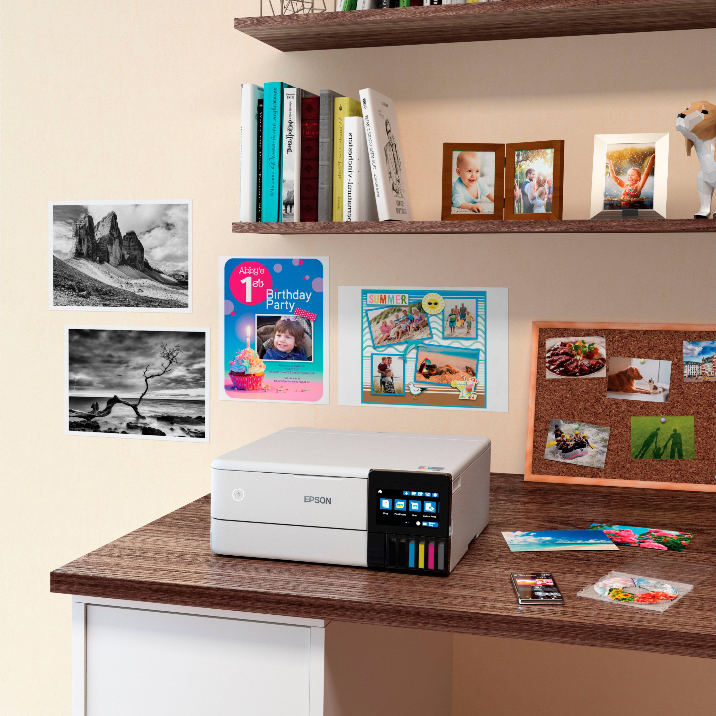 The image features a white desk with a printer on it. The printer is surrounded by a variety of items, including books, pictures, and a corkboard. There are also several children's birthday party invitations displayed on the wall. The scene appears to be a home office or a workspace where someone might use the printer for various tasks, such as printing photos or documents.