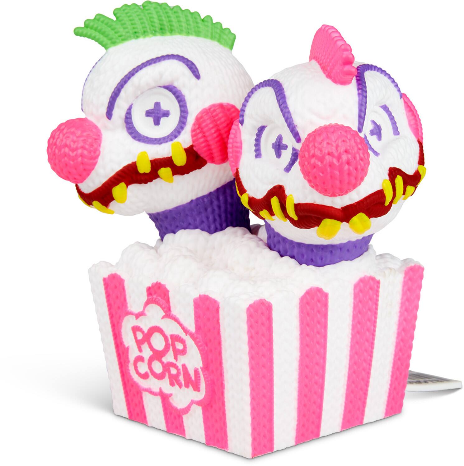 The image shows two plush clown toys with green and pink hair, sitting on a popcorn box. The box is white with pink stripes and has the text "POP CORN" on it.