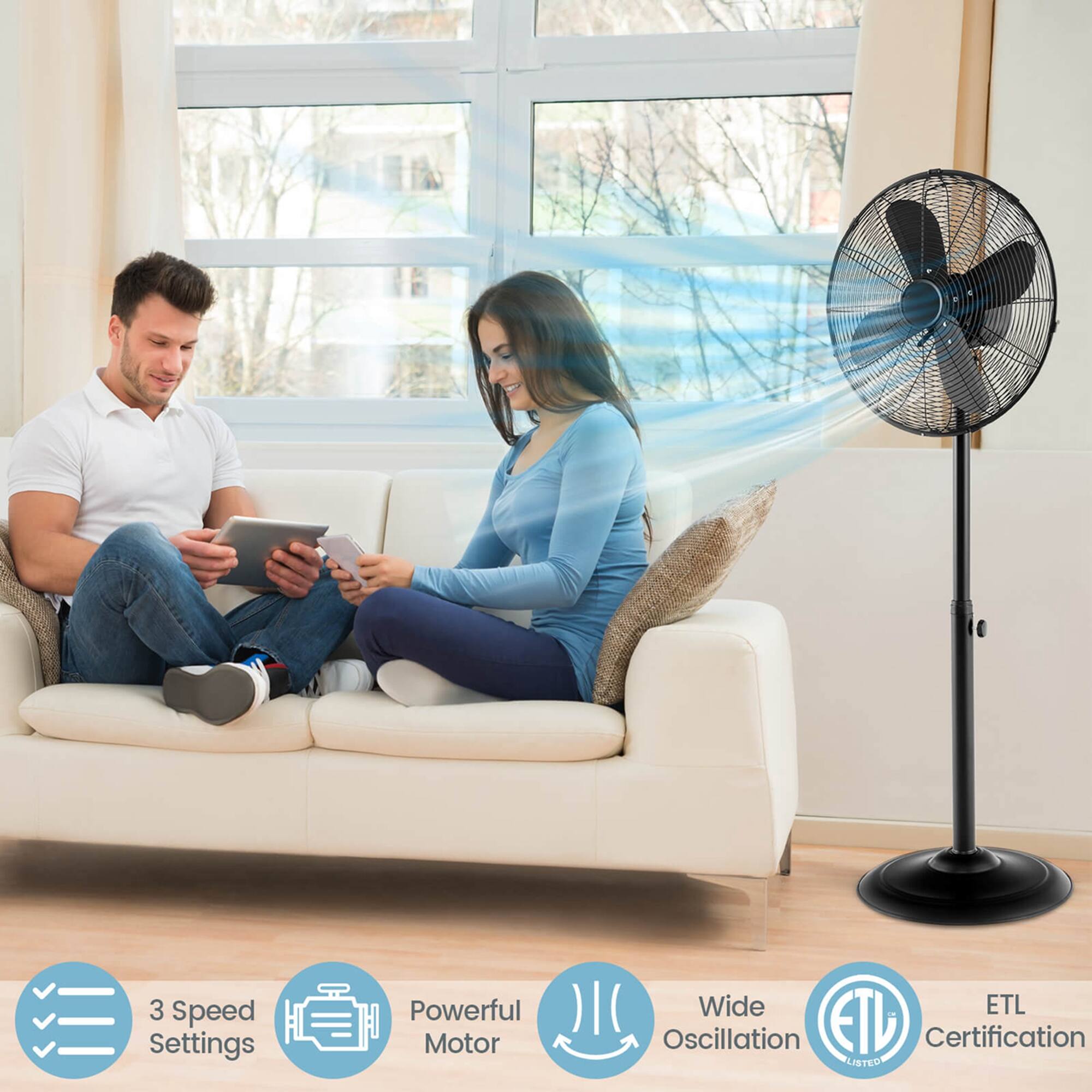 The image features a man and a woman sitting on a couch, each holding a tablet. They are surrounded by a black fan, which is placed on the floor near the couch. The fan has a blue light, and it is described as having 3 speed settings, a powerful motor, and wide ETL oscillation. The fan is also certified by ETL.