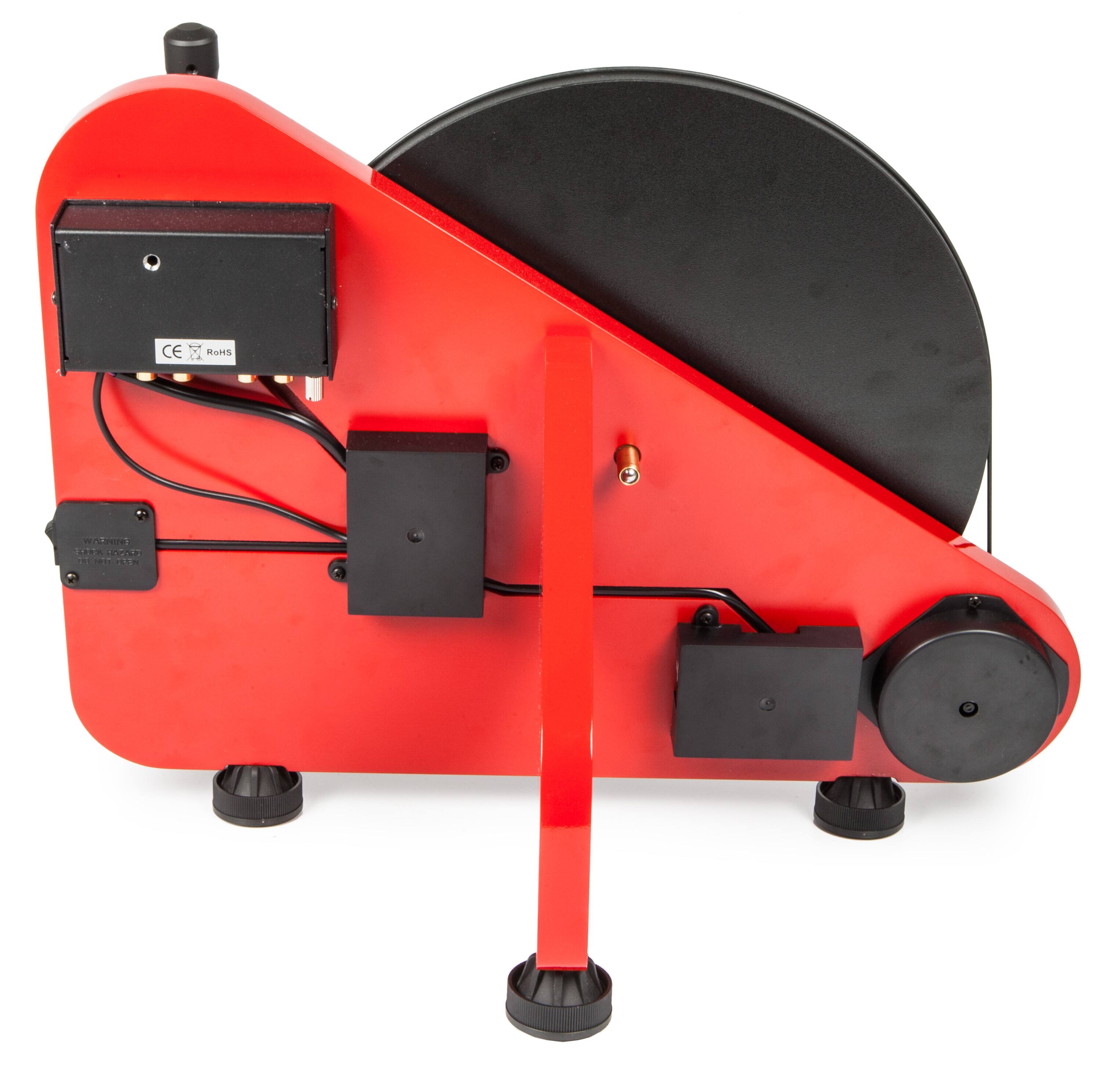 The image features a red machine with a black and red wheel, possibly a toy or a piece of equipment. The machine has a red handle, and there is a black box with a red wheel attached to it. The machine is placed on a white background, making it stand out prominently.