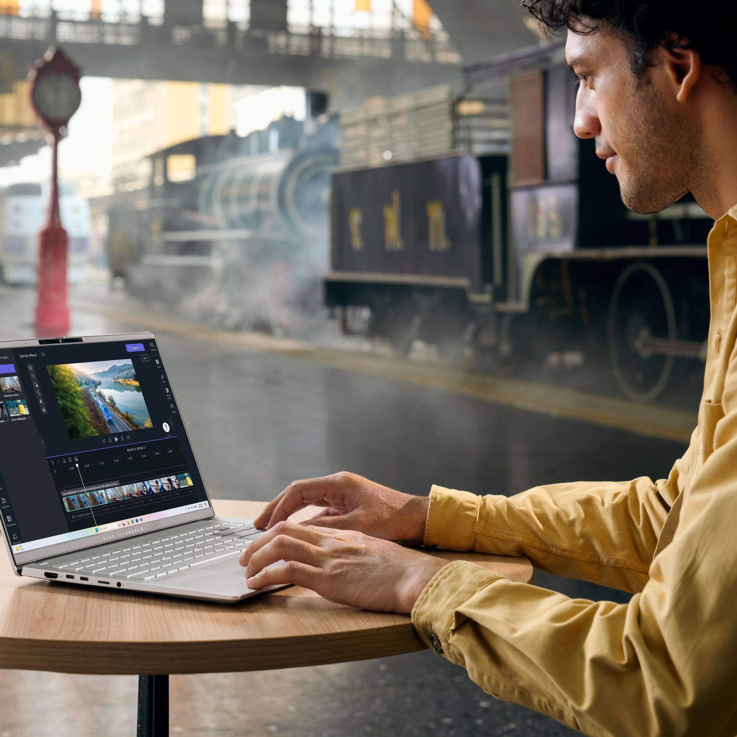 The text on the image reads: "A man is working on a laptop computer at a table. He is sitting in front of a train, which is passing by. The man is focused on his work, and the train is in the background."