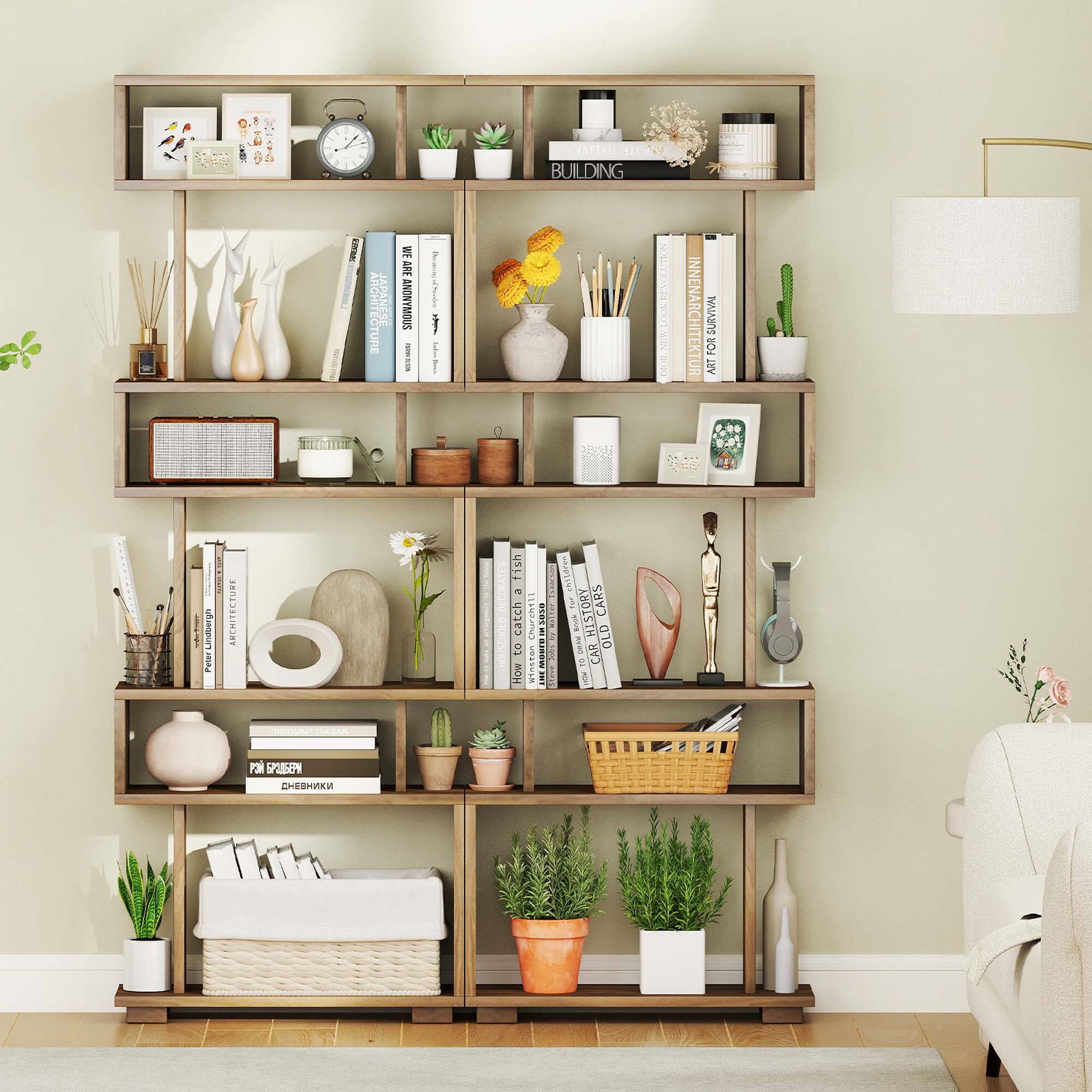 The image features a bookshelf filled with various items, including books, potted plants, vases, and a clock. There are at least 12 books on the shelf, with some placed on the top and others on the bottom. The bookshelf also has a few vases, with one located at the top left and another at the top right. Additionally, there are two potted plants, one on the left side and another on the right side of the shelf. A clock can be seen hanging on the wall above the bookshelf. The shelf is placed in a living room, and there is a couch in the background.