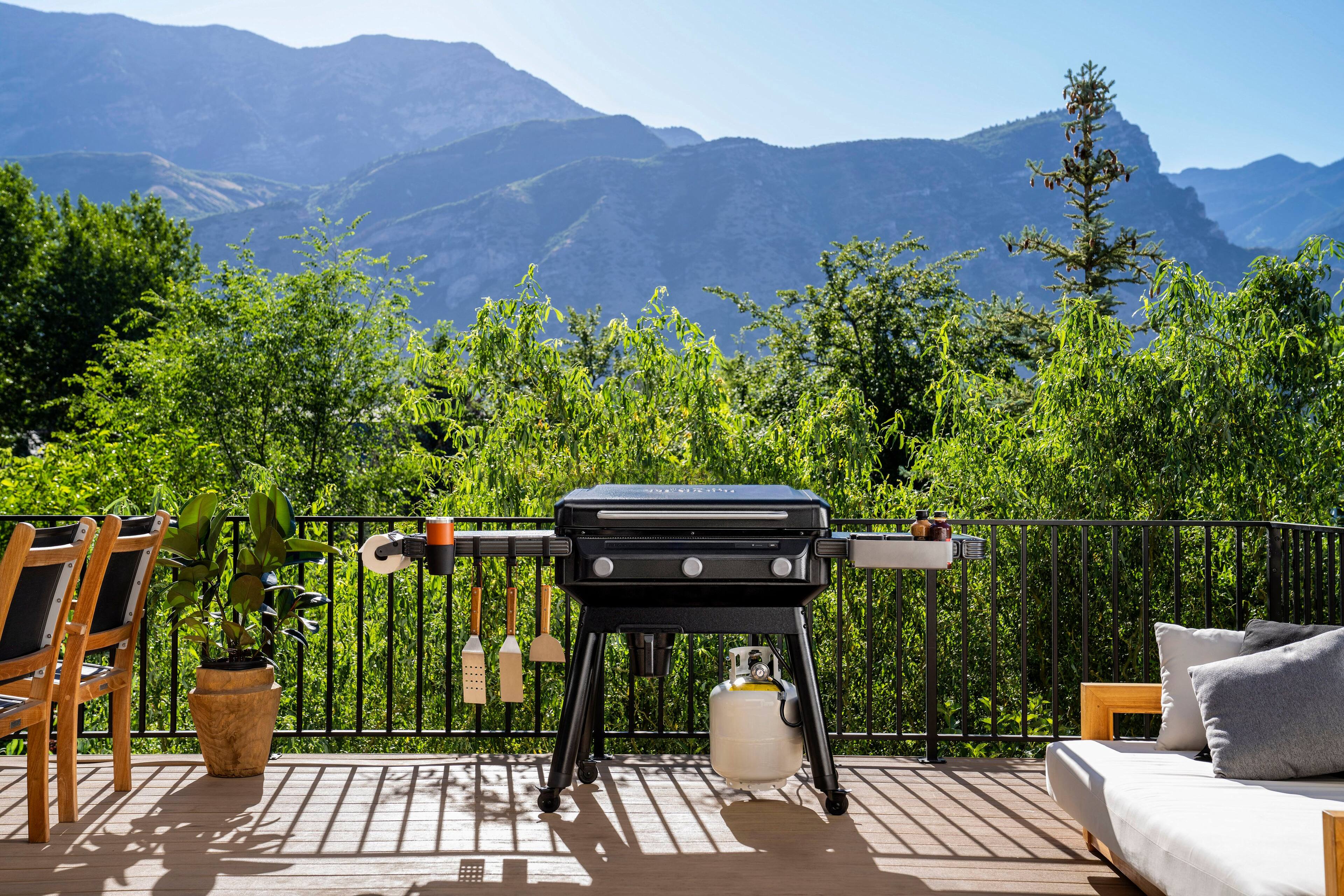 The image features a deck with a grill, a table, and chairs. The grill is set up on the deck, and there are two chairs and a table nearby. The deck overlooks a beautiful mountain view, making it an ideal spot for outdoor cooking and dining. The grill is surrounded by a fence, providing a sense of safety and containment. The scene is perfect for a relaxing day outdoors, enjoying the scenic view while grilling food and spending time with friends or family.