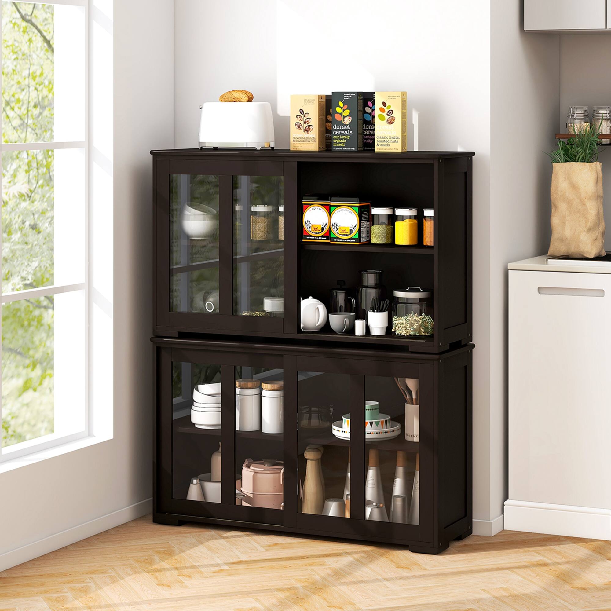 The image shows a kitchen with a black cabinet and a window. The cabinet is filled with various items, including a toaster, cups, bowls, and bottles. There are also several spices and other kitchen essentials stored in the cabinet. The cabinet is placed next to a refrigerator, and a potted plant can be seen nearby. The scene appears to be a well-organized and functional kitchen space.