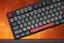 The text on the image is in a foreign language, so it is not possible to group and correct it without understanding the language. However, I can provide some general information about the keyboard layout.

The keyboard in the image has a unique layout with several non-standard keys. It has a red key on the left side, which is likely the Shift key. The rest of the keys are arranged in a way that is not typical of standard keyboards. The keys are likely designed for a specific language or purpose, as the layout deviates from the standard QWERTY or AZERTY layouts.
