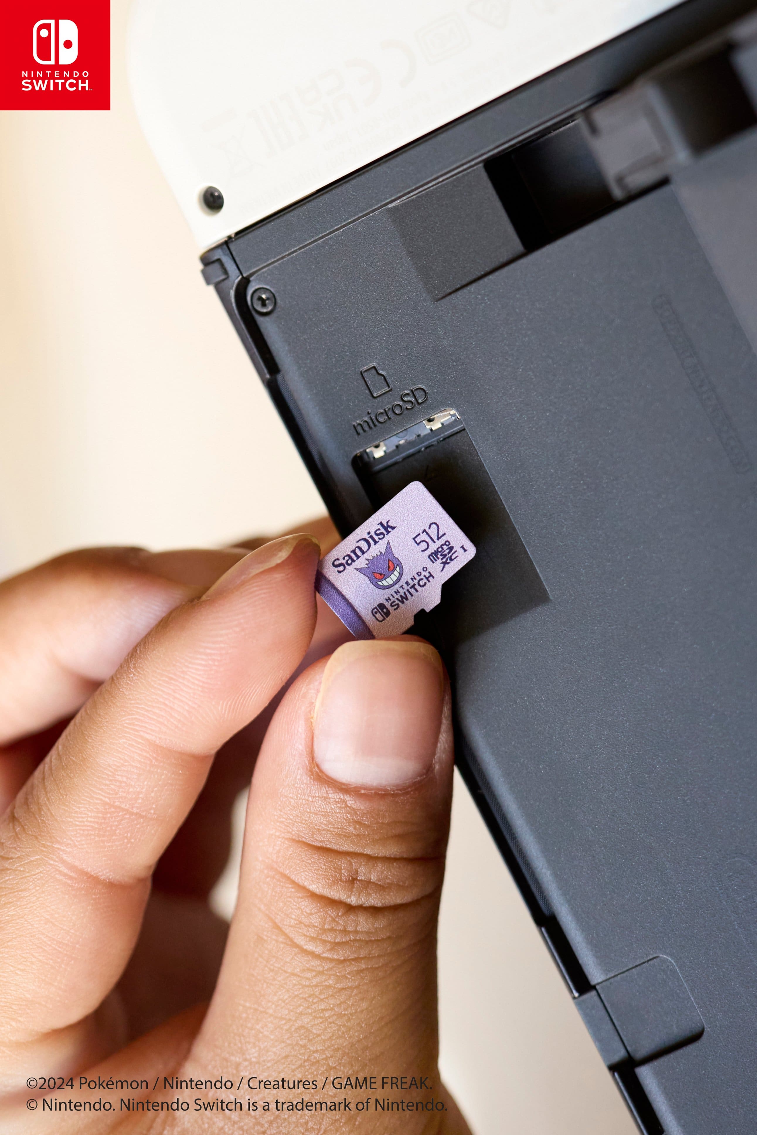Nintendo Switch is a trademark of Nintendo. The image features a hand holding a microSD card, which is being inserted into a Nintendo Switch. The card is a SanDisk 512 GB microSD card.
