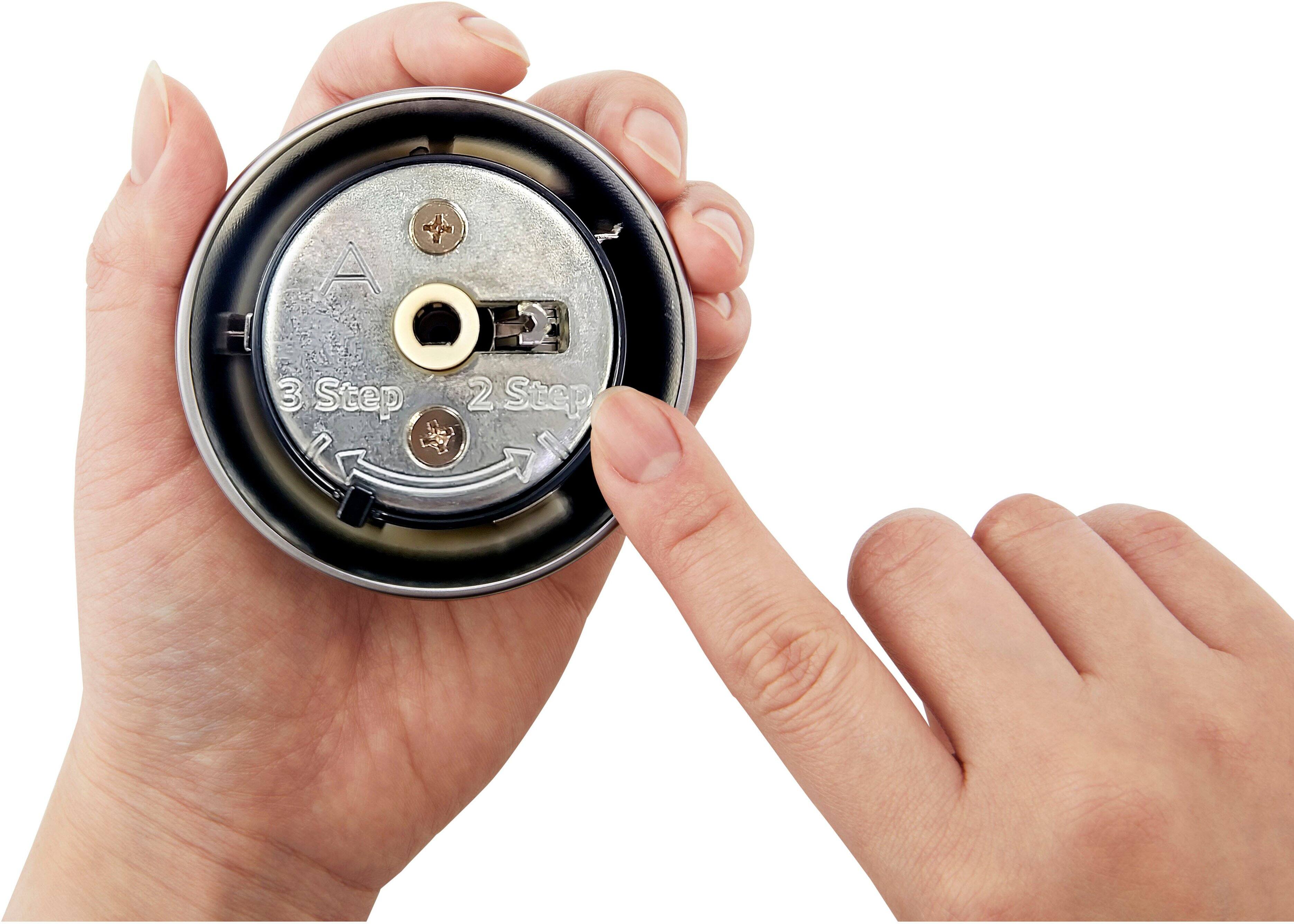 A person is holding a small object, possibly a watch or a small machine, in their hands. The object has a dial and a button on it, and the person is examining it closely. The image description suggests that the person is in the process of disassembling or repairing the object, as they are holding it with their hands and looking at it closely.