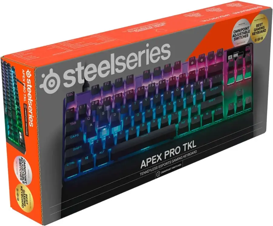 The image features a close-up of a Steelseries Apex Pro TKL keyboard. The keyboard is designed with a tenkeyless layout, making it a compact and space-saving option for gamers and users. The Apex Pro TKL keyboard is known for its adjustable switches, which allow users to customize the feel and responsiveness of the keys. The keyboard is packaged in a box, showcasing its features and design.