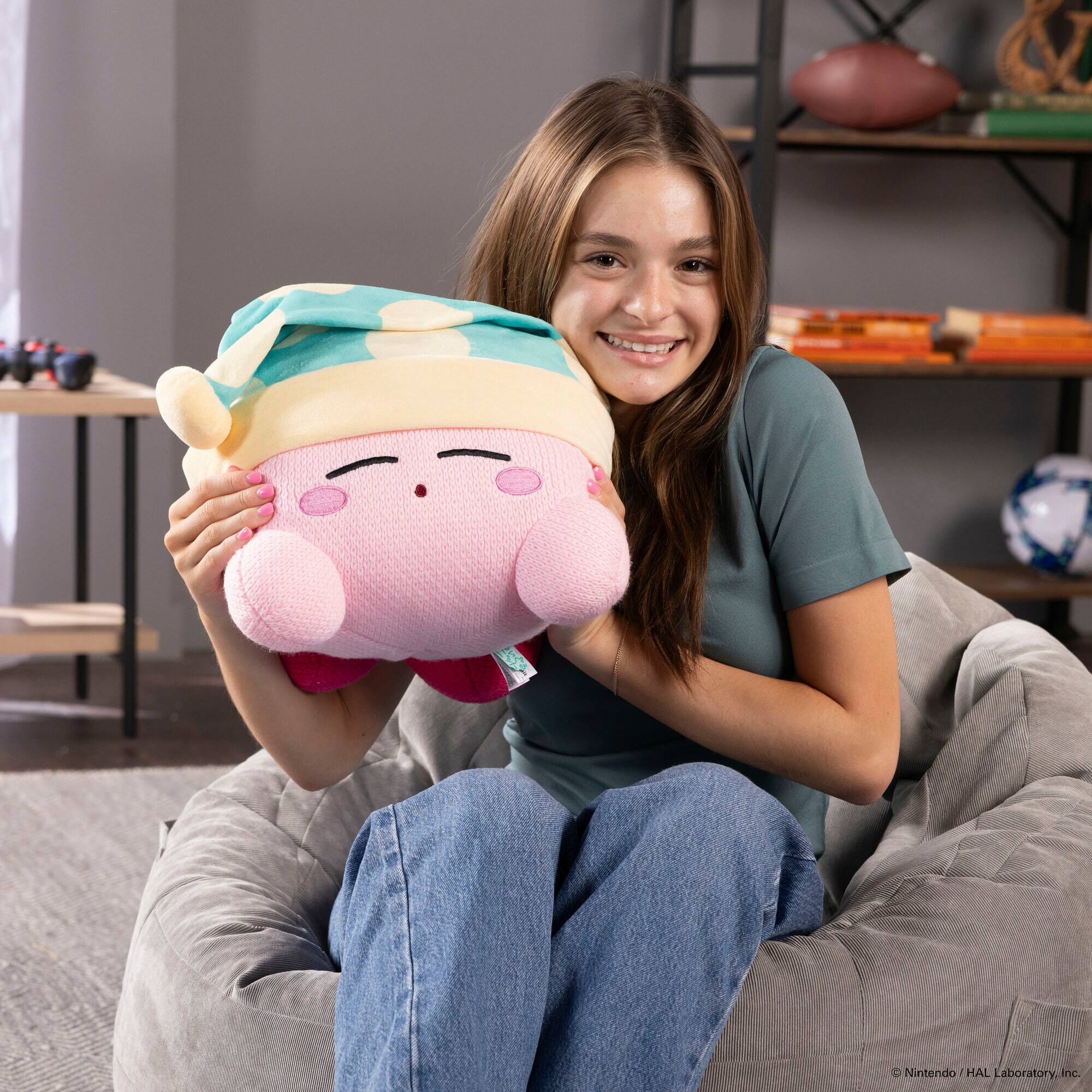 The image shows a woman sitting on a chair and holding a pink stuffed animal, which is a Nintendo character. The text on the image reads "6 C Nintendo/HAI HAL Laboratory. Inc." This suggests that the stuffed animal is a product of Nintendo and HAI HAL Laboratory, Inc.