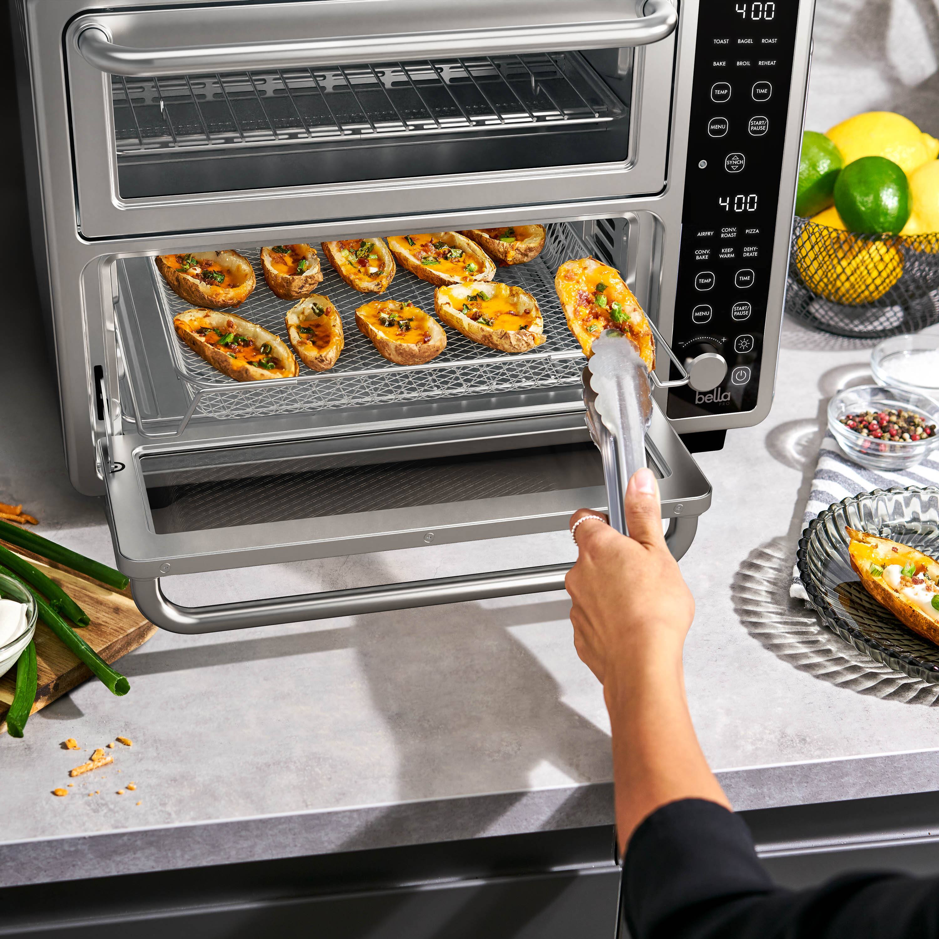 The image shows a person using a toaster oven to cook food. The toaster oven is filled with food, and the person is reaching in to take out a piece of food. The oven is placed on a countertop, and there are several pieces of broccoli nearby. The person is wearing a black shirt, and the scene appears to be set in a kitchen.