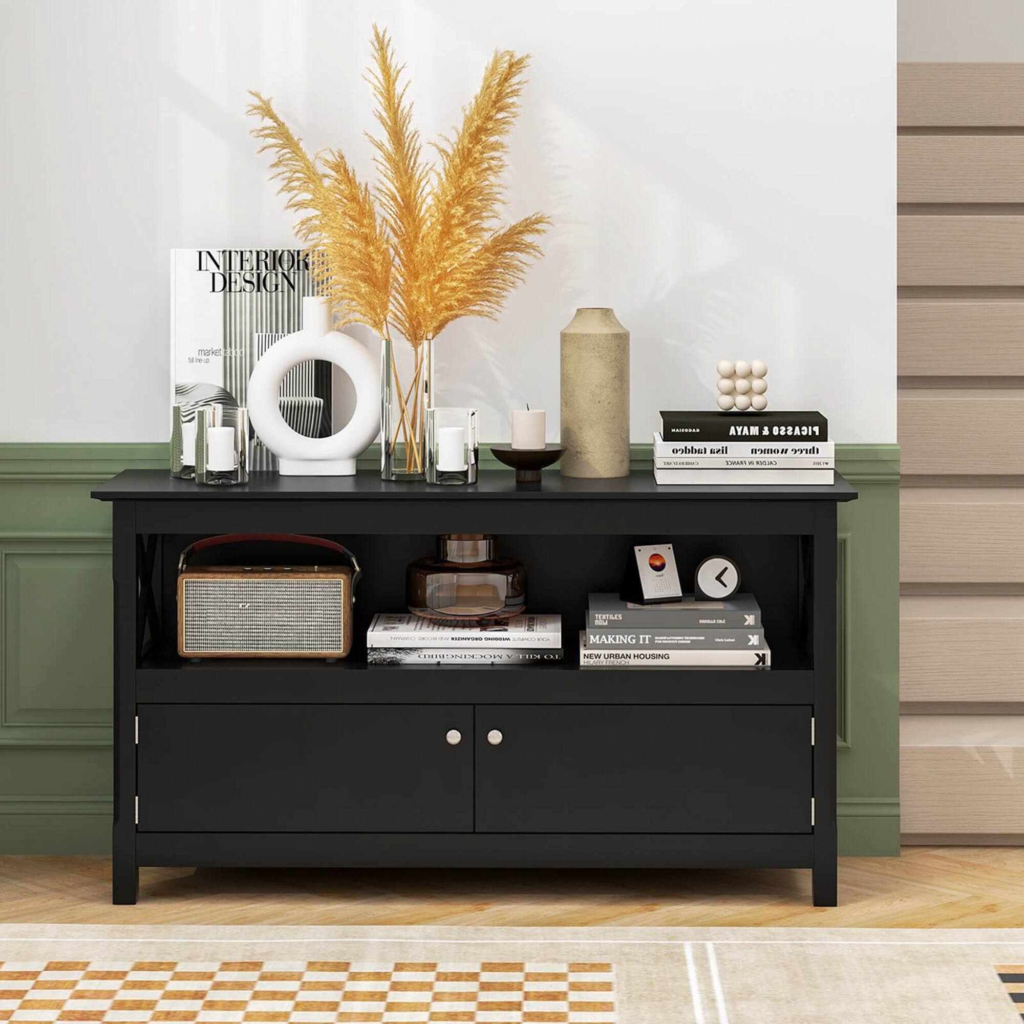 The image features a black table with various items on it. There is a vase with a plant, a stack of books, a clock, and a radio. The table is situated next to a wall, and there is a window nearby. The arrangement of the items on the table creates a cozy and functional space for everyday use.
