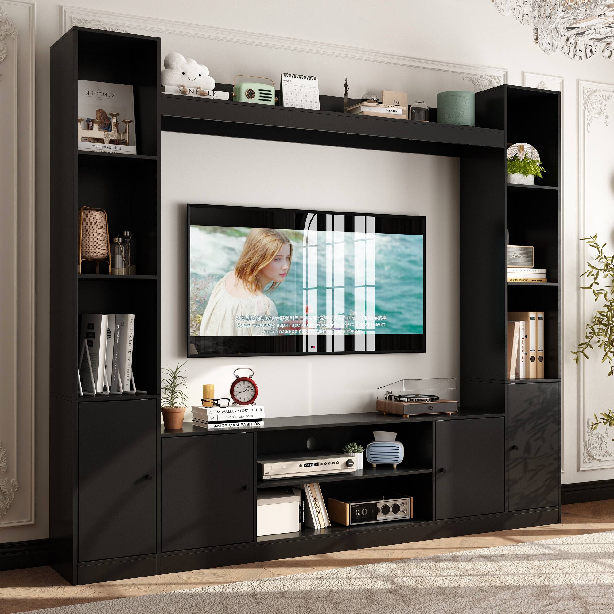 The image features a living room with a large flat screen TV mounted on the wall. The room is furnished with a black entertainment center and a bookshelf. There are several books placed on the bookshelf, and a clock can be seen on the wall. Additionally, there are two potted plants in the room, one near the TV and the other near the bookshelf. The room also has a vase and a teddy bear, adding to the cozy atmosphere.