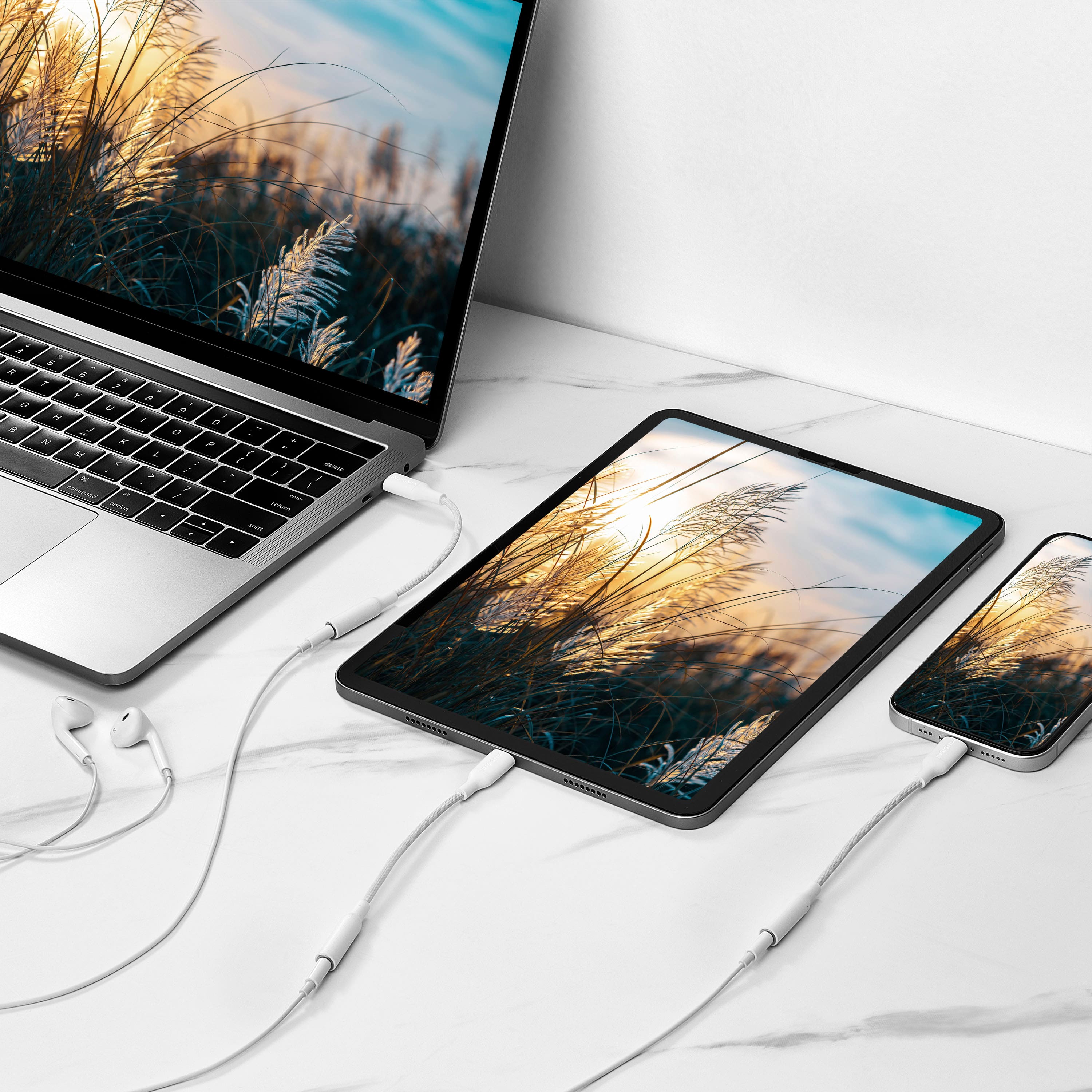 The image shows a laptop and two tablets placed on a white table. The laptop is connected to the tablets, which are charging. The tablets are placed side by side, with one on the left and the other on the right. The laptop is positioned in the middle, with its screen facing the tablets. The arrangement suggests that the devices are being used in a multi-screen setup, possibly for work or entertainment purposes.
