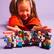 The image shows a young girl sitting on the floor with a large group of Lego characters. She is surrounded by various Lego figures, including some that are placed on the floor in front of her. The girl appears to be enjoying her time with the Lego toys, possibly playing or organizing them.