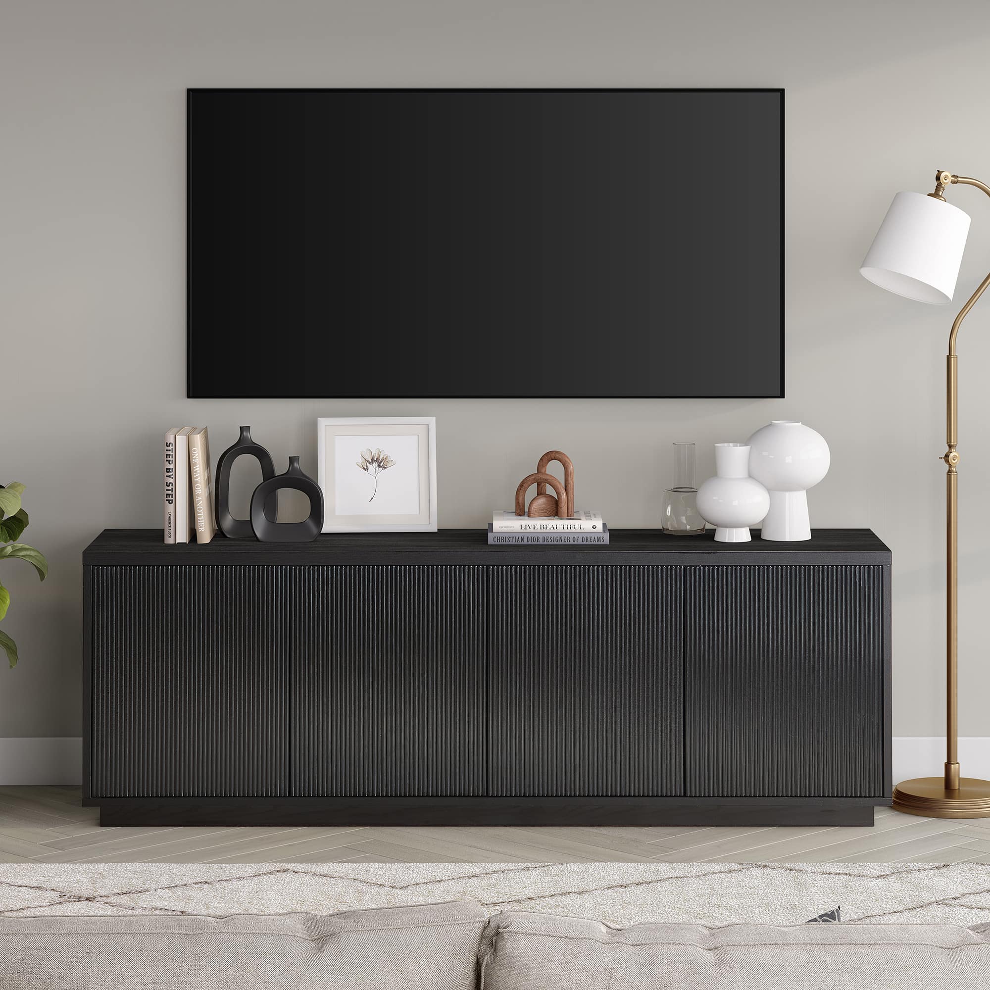 The image shows a living room with a flat screen TV mounted on the wall. The room also features a wooden entertainment center with a lamp on it. There are several books placed on the entertainment center, and a vase is also present in the room. The room appears to be well-organized and ready for entertainment.