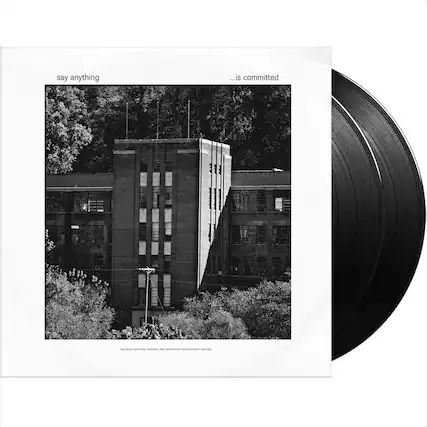 The image features a large brick building with many windows. The album cover for Say Anything is displayed, which says "is committed." The cover is black and white, and the building serves as the background for the album cover.
