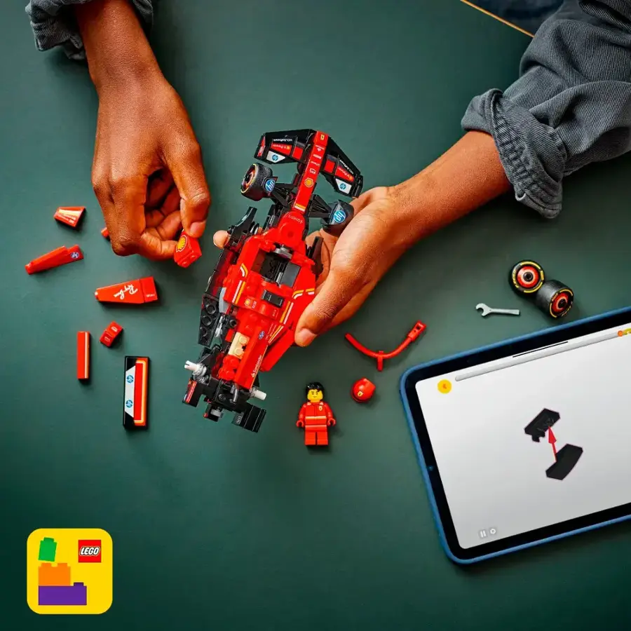 A person is building a Lego car on a table. They are using a Lego car set and a tablet to help them with the construction. The tablet is displaying instructions for the Lego car, and the person is holding the car together with their hands.