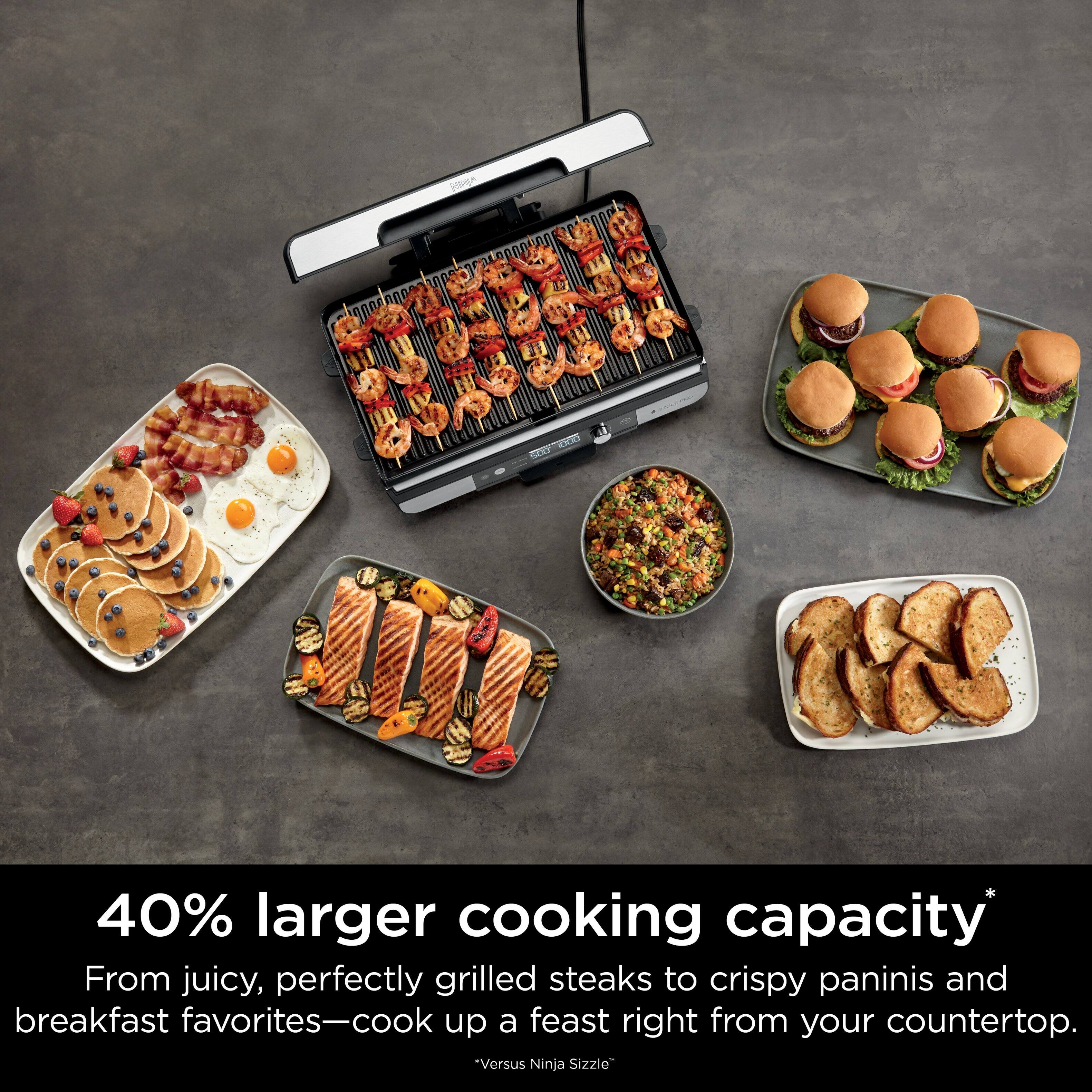 The image features a variety of food items, including sandwiches, pancakes, and grilled steaks, all displayed on a countertop. The text on the image suggests that the cooking appliance has a 40% larger cooking capacity compared to the Ninja Sizzle, allowing for more versatile and efficient cooking options. This appliance is ideal for preparing a wide range of dishes, from delicious breakfast items to crispy paninis and juicy grilled steaks.