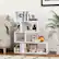 The image features a white bookshelf filled with various items, including books, a vase, a potted plant, and a teddy bear. The bookshelf is situated next to a couch, and there is a picture on the shelf. The scene is set in a living room, with a cozy and inviting atmosphere.