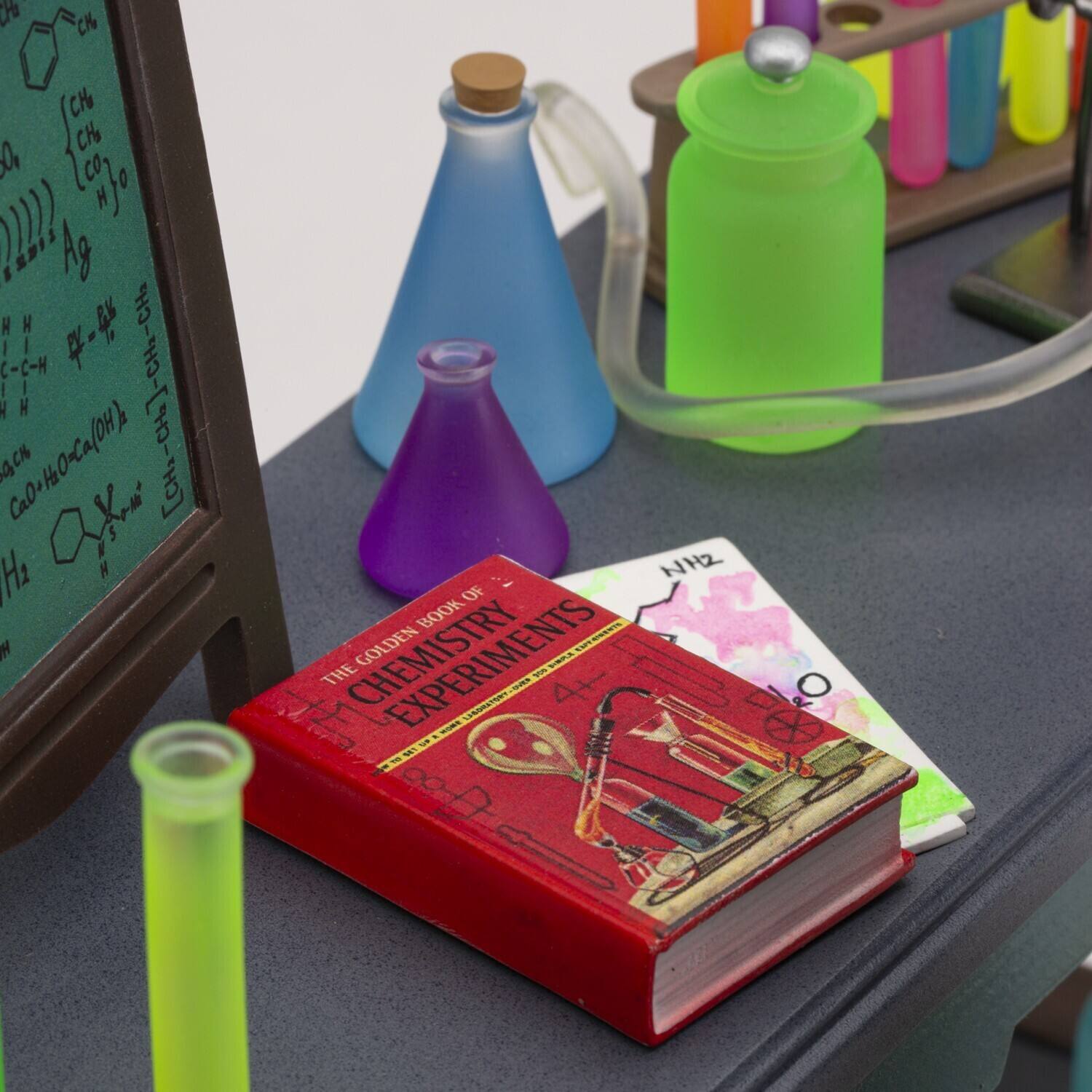 Sure, here is the corrected and grouped text from the image:

**On the Blackboard:**
- C6H5COOH
- [CH3CH2COO]n
- Ag
- H2C=CH2
- CaO + H2O → Ca(OH)2
- NH2

**On the Book:**
- THE GOLDEN BOOK OF CHEMISTRY EXPERIMENTS

**On the Paper:**
- NH2

**Other Text:**
- nJo
- 2 HAg
- H HH H CH2
- C-C-H
- Ca0HO-Ca(OH)
- N H
- NH2
- OF BOOK GOLDEN no EXPERIMENTS
- THE GOLDEN BOOK OF CHEMISTRY EXPERIMENTS