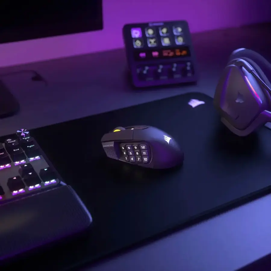 The image shows a computer desk with a mouse, keyboard, and a monitor. The mouse is placed on a mouse pad, and there is a purple background. The keyboard is positioned in front of the mouse, and the monitor is located on the left side of the desk. The desk also has a clock and a small speaker on it.