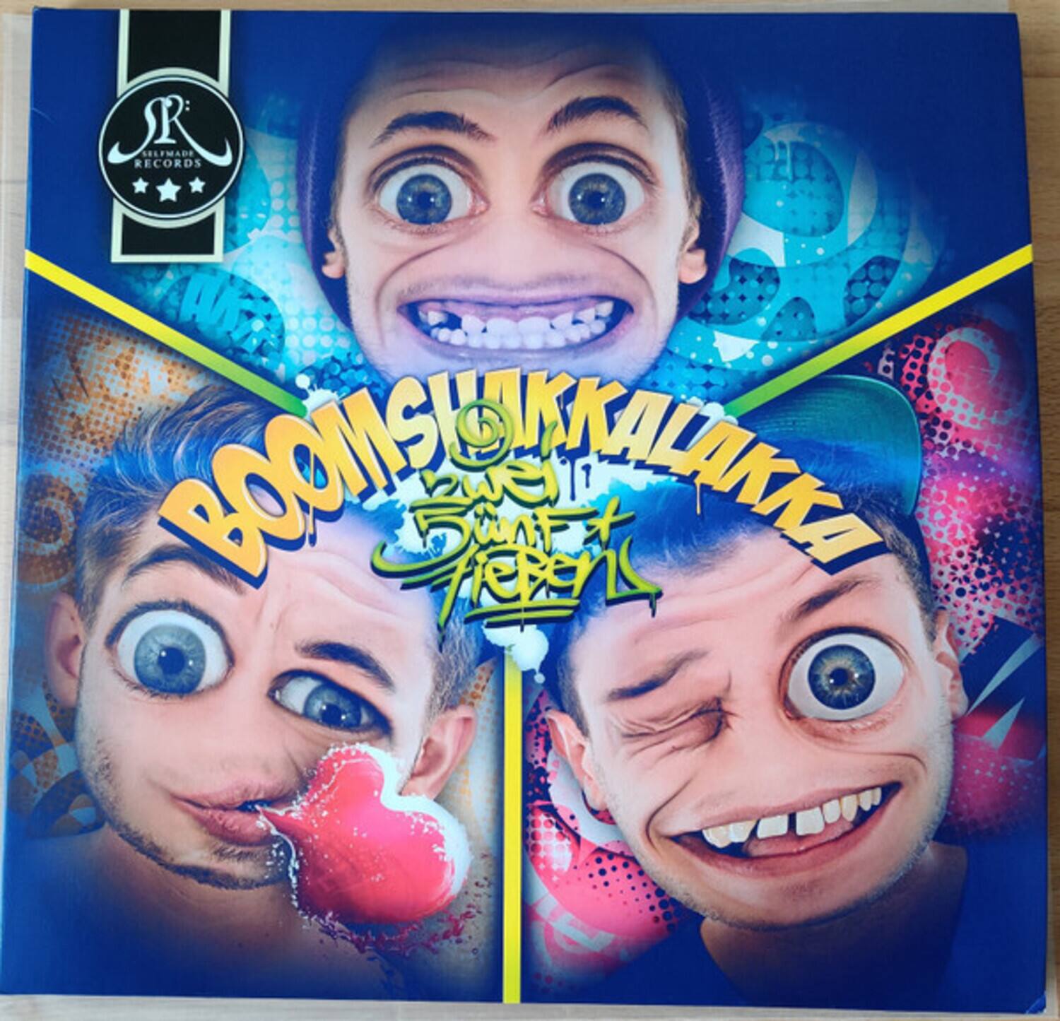 Sure, here is the corrected and grouped text from the image:

---

**R**  
**SELFMADE RECORDS**

**BOOMSHAKKALAKKA**  
**SUN FRIEST**

---

The text is arranged as follows:

- At the top left corner: "R" with "SELFMADE RECORDS" below it.
- In the center: "BOOMSHAKKALAKKA" with "SUN FRIEST" below it.