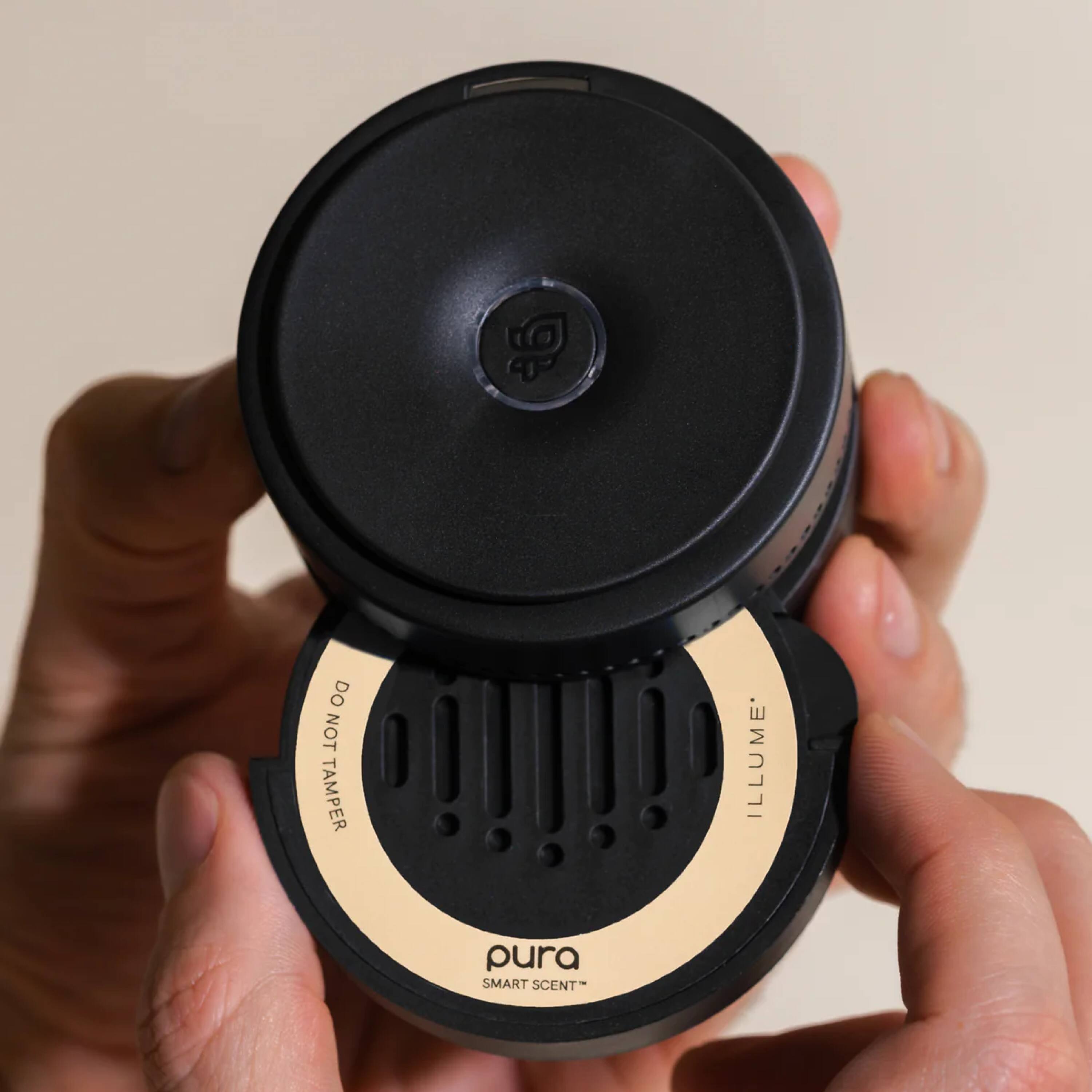 "Do not tamper" is a warning that the person should not interfere with the device or its components. The device is an illume pura smart scent, which is a scent diffuser. The person is holding the device in their hand, and it is important to follow the instructions to ensure proper functioning and avoid potential damage.