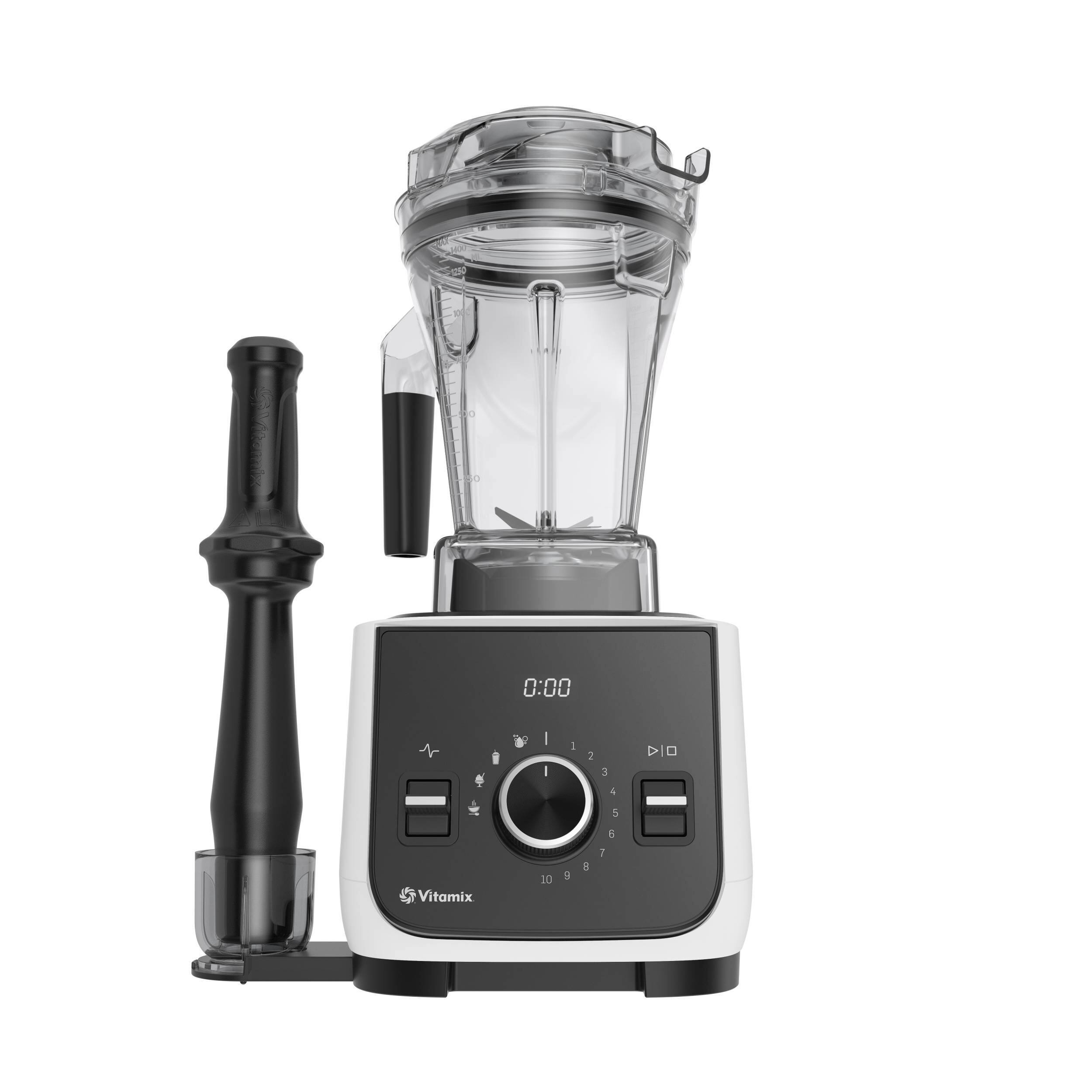 The image features a Vitamix blender with a black handle and a black blade. The blender is sitting on a white countertop. The blender is turned on, with the timer set at 0:00.