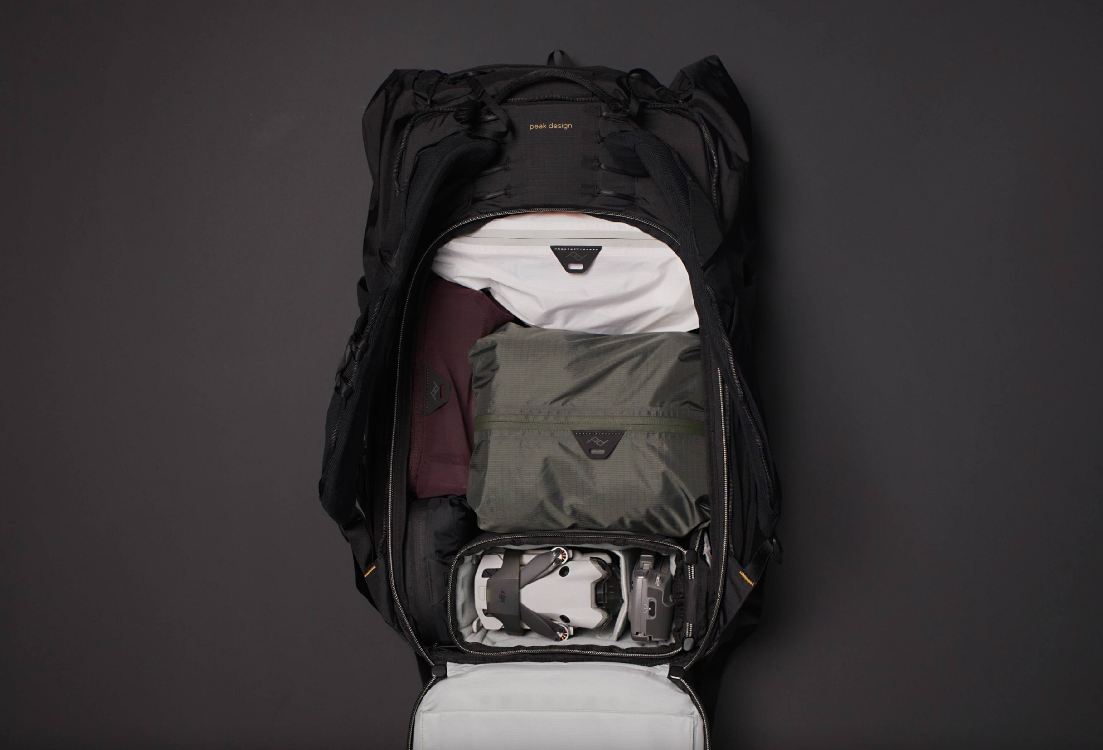 Peak Design is a company that specializes in creating high-quality, durable, and functional outdoor gear, such as backpacks and camera bags. The image shows a backpack with its contents visible, including a camera bag, a laptop case, and a toiletry bag. The backpack is open, revealing the items inside, which are neatly organized and ready for use.
