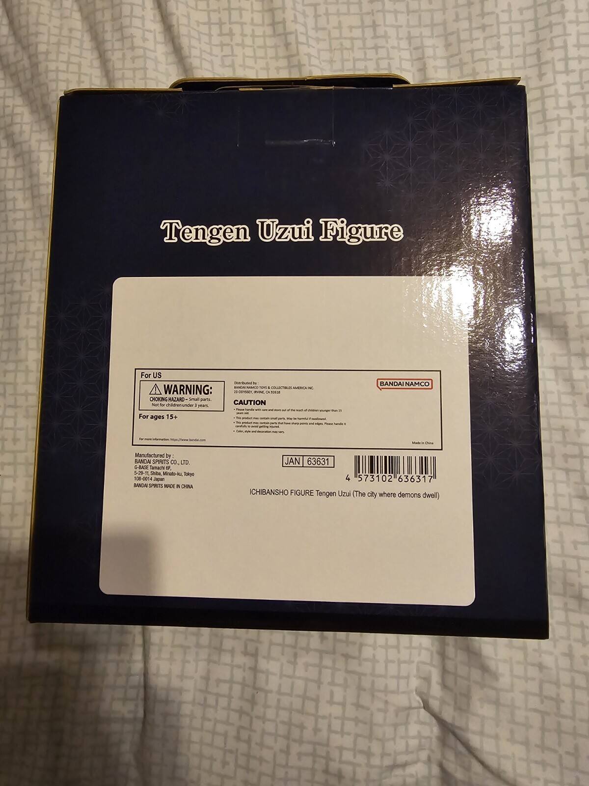 The text on the image can be grouped and corrected as follows:

---

**Tengen Uzui Figure**

**For US**

**WARNING:**

- CHOKING HAZARD - Small parts. Not for children under 3 years.

**CAUTION:**

- For ages 15+

---

**BANDAI NAMCO**

Manufactured by BANDAI SPIRITS CO LTD

5-29-11 Shiba Minato, Tokyo 108-0014

**JAN 63631 4 573102 636317**

**ICHIBANSHO FIGURE Tengen Uzui (The city where demons dwell)**

---

**Made in China**