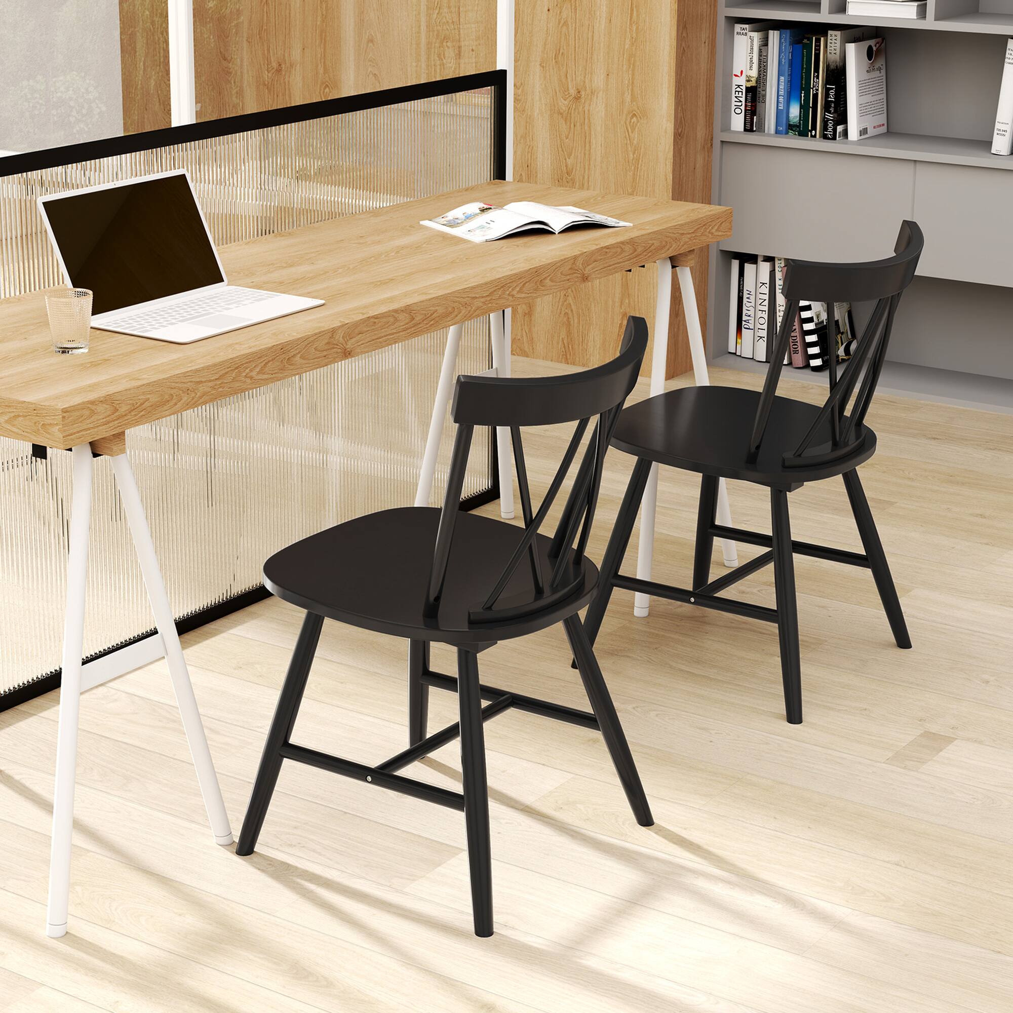 The image features a wooden table with a laptop and two black chairs. The table is surrounded by books, and there is a glass of water nearby. The chairs are positioned on either side of the table, creating a comfortable workspace. The overall scene suggests a cozy and functional home office setup.