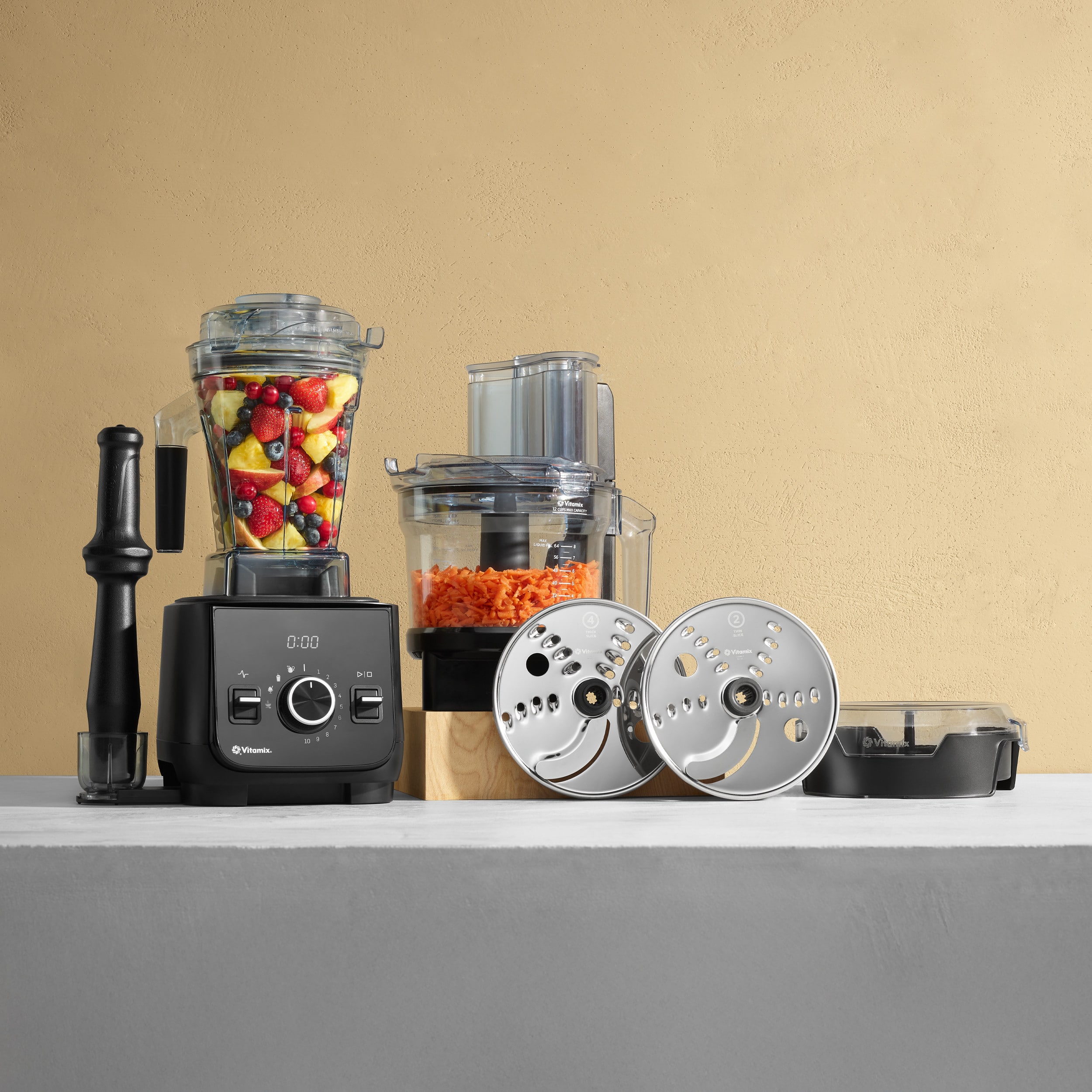 The image features a counter with various kitchen appliances and food items. There is a blender, a food processor, and a juicer, all of which are filled with different ingredients. The blender contains fruit, while the food processor has carrots and the juicer has carrots and a juice. The counter also has a bowl and a spoon, indicating that the food is ready to be consumed. The scene suggests that someone is preparing a meal or a drink using these appliances and ingredients.