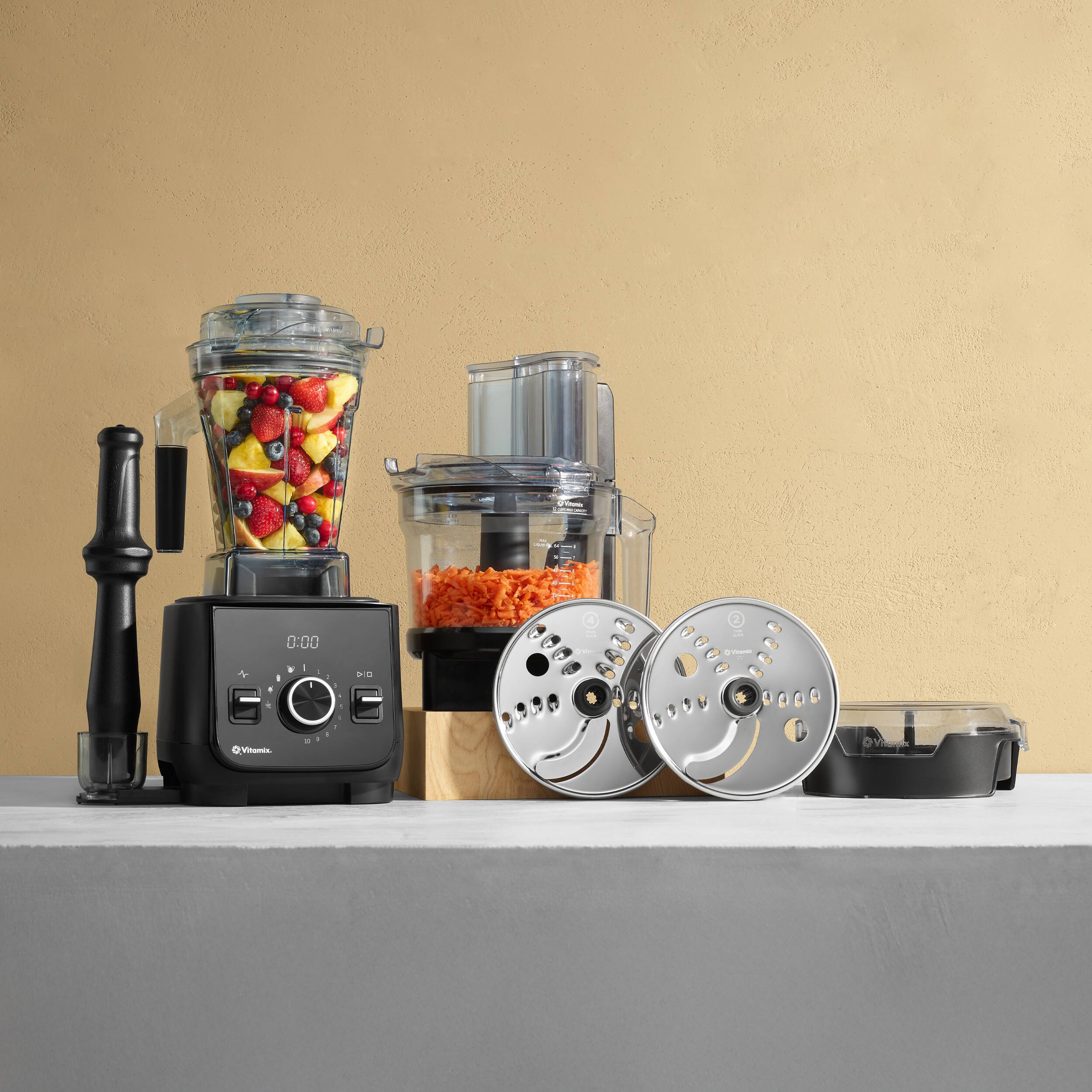 The image features a counter with various kitchen appliances and food items. There is a blender, a food processor, and a juicer, all of which are filled with different ingredients. The blender contains fruit, while the food processor has carrots and the juicer has carrots and a juice. The counter also has a bowl and a spoon, indicating that the food is ready to be consumed. The scene suggests that someone is preparing a meal or a drink using these appliances and ingredients.