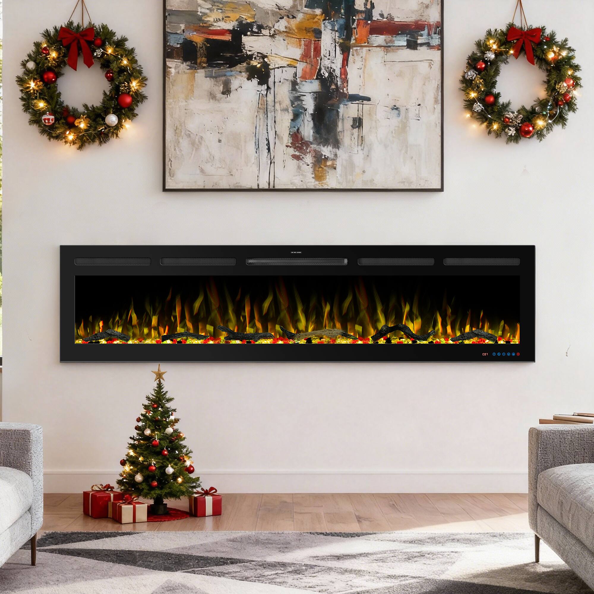 The image shows a cozy living room decorated for Christmas. There is a large abstract painting above a modern electric fireplace. On either side of the painting, there are two wreaths with red bows and Christmas lights. Below the fireplace, there is a small Christmas tree adorned with red and white ornaments and a star on top. Under the tree, there are wrapped presents. The room has a light and festive atmosphere.