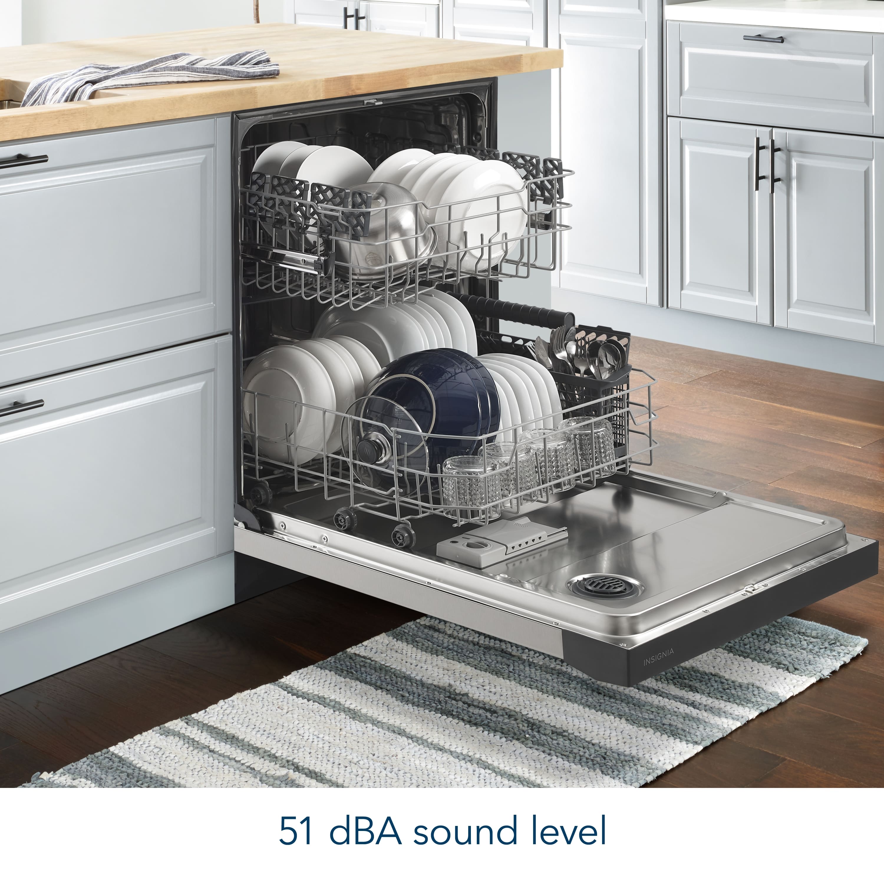 The image shows a kitchen with a dishwasher that operates at a sound level of 51 dBA. The dishwasher is filled with dishes, including plates and bowls, and is placed under a counter. The kitchen also features a sink and cabinets.