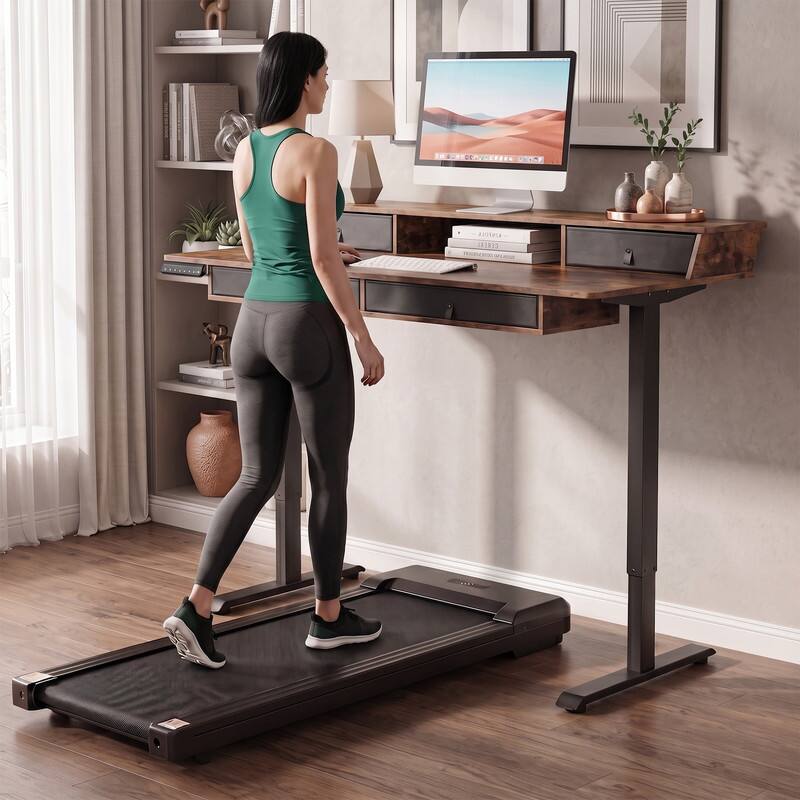 In a room, a woman is using a treadmill while working on a computer.