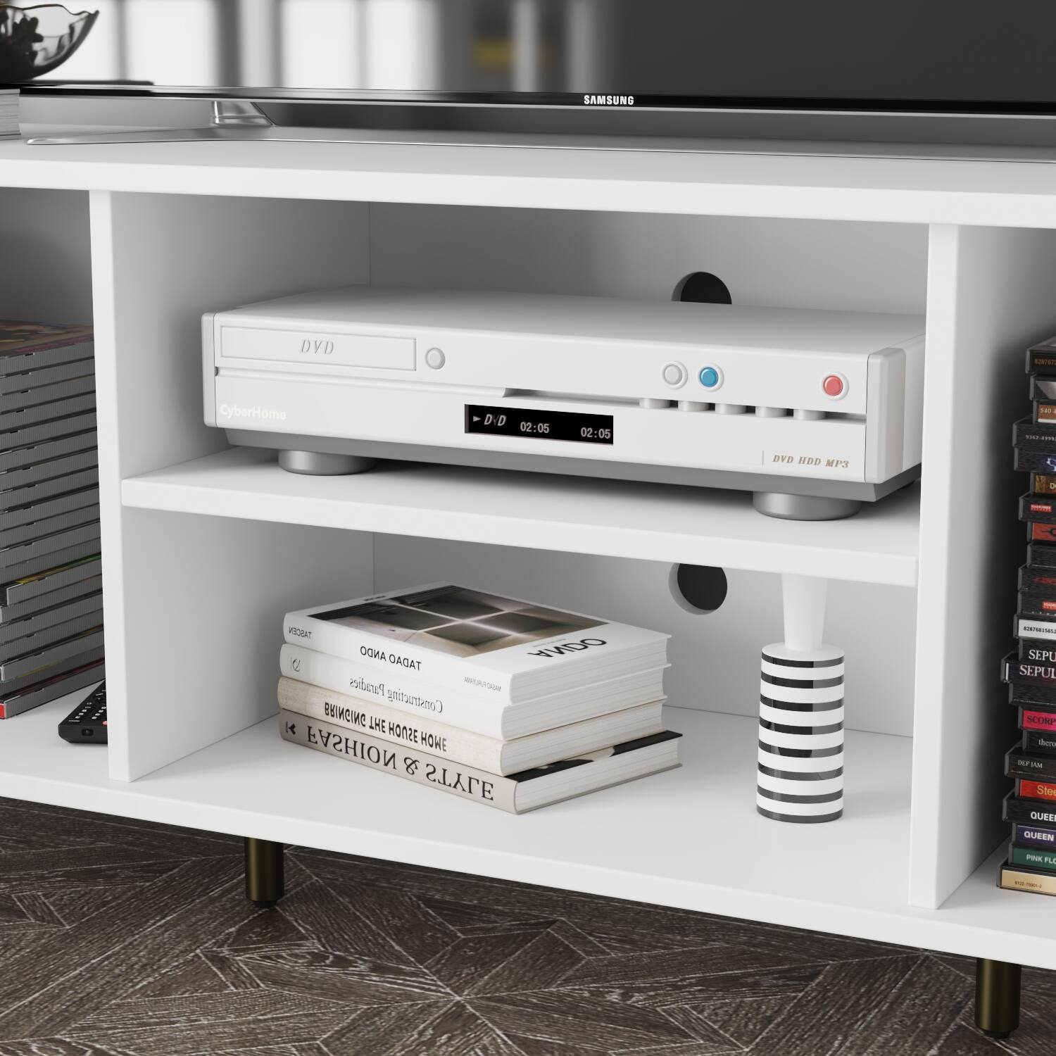 The image features a white shelf with various items on it. There is a Samsung DVD player on the shelf, along with a collection of books and a remote control. The books are arranged in a stack, and the remote control is placed nearby. The shelf is located in a living room, providing a convenient space for storing and displaying these items.