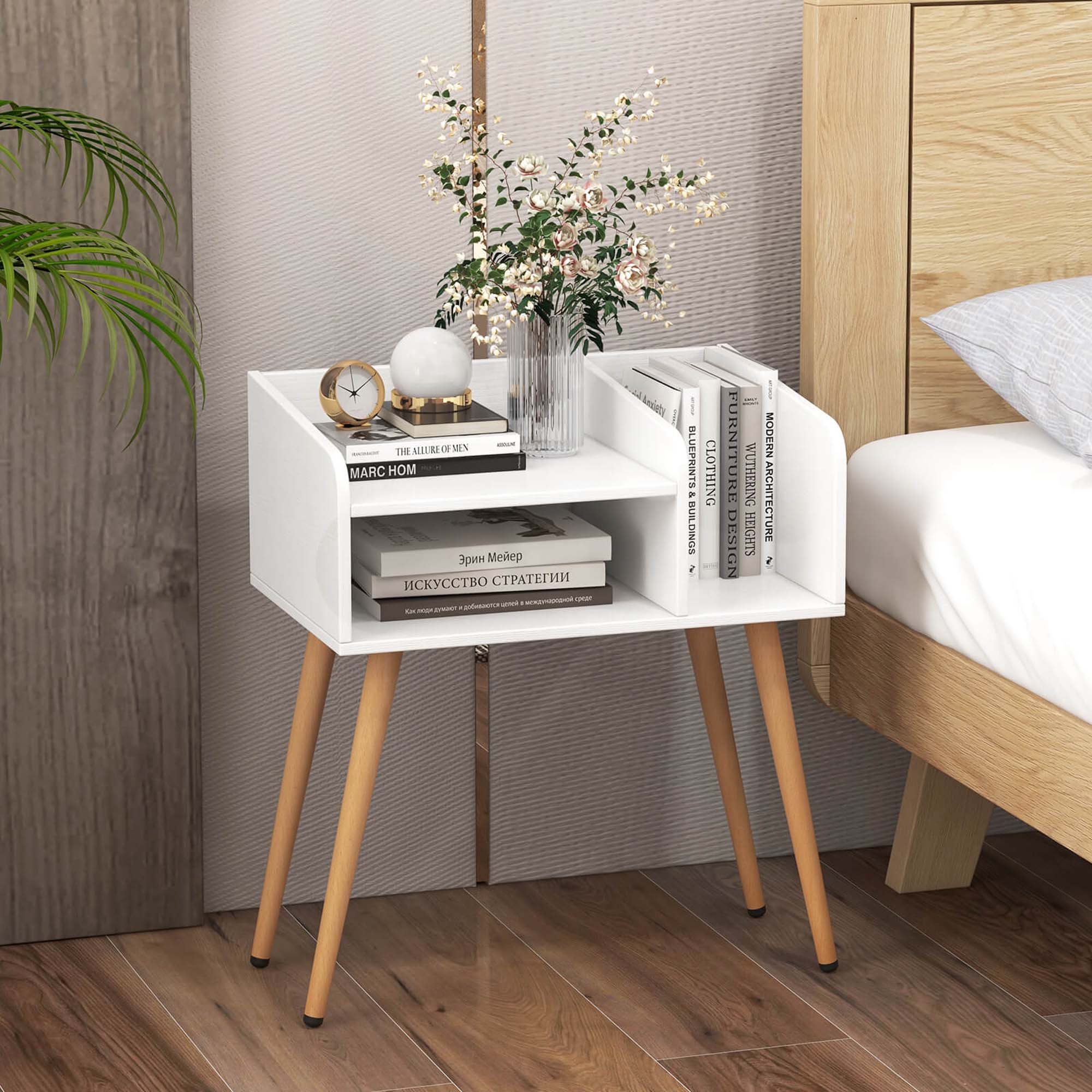 The image features a white nightstand with a clock on it. The nightstand is placed next to a bed, which has a white comforter. There is also a small table with a vase of flowers on it, adding a touch of elegance to the room. The nightstand is accompanied by a bookshelf with several books on it, providing a cozy and functional space for reading and relaxation.