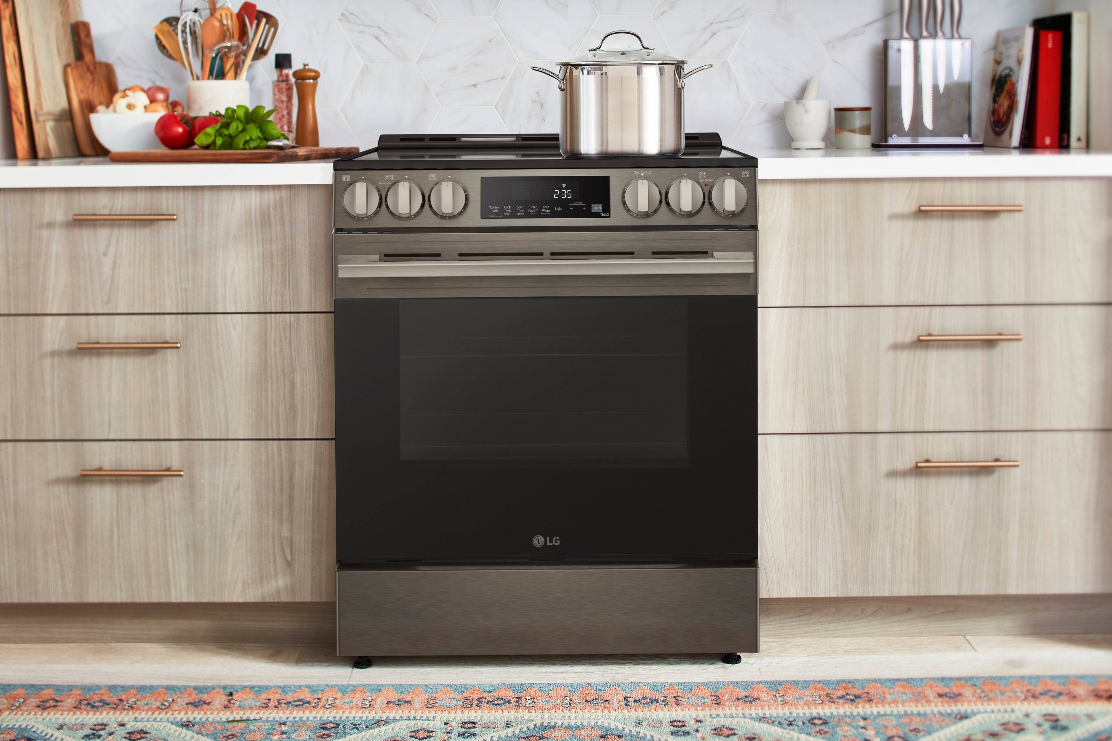 The image shows a kitchen with a stove top oven, which has the time 2:35 displayed on it. The oven is surrounded by cabinets, and there are various kitchen items nearby, such as a bowl, a knife, a spoon, and a bottle. Additionally, there are some apples and a book in the scene.