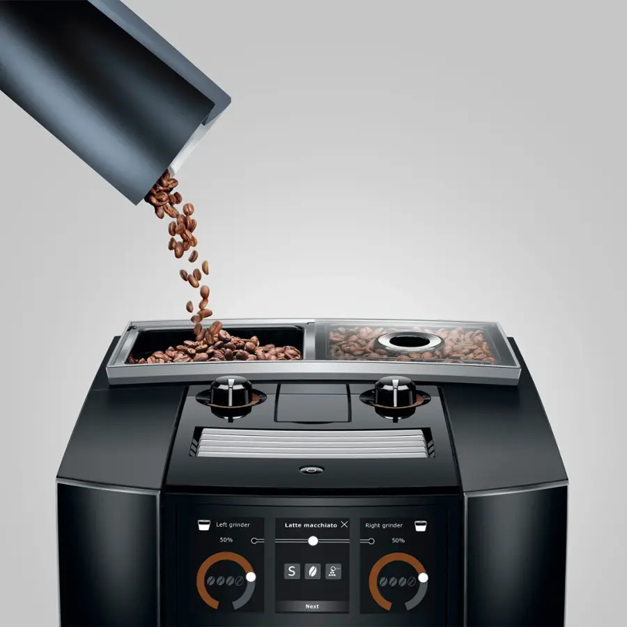 The image shows a coffee grinder with beans being poured into it. The grinder has a left and right side, and the beans are being evenly distributed between the two sides. The left grinder is set to 50%, while the right grinder is set to 50%, ensuring a balanced grinding process. The beans are being poured into the grinder to create a delicious latte macchiato.